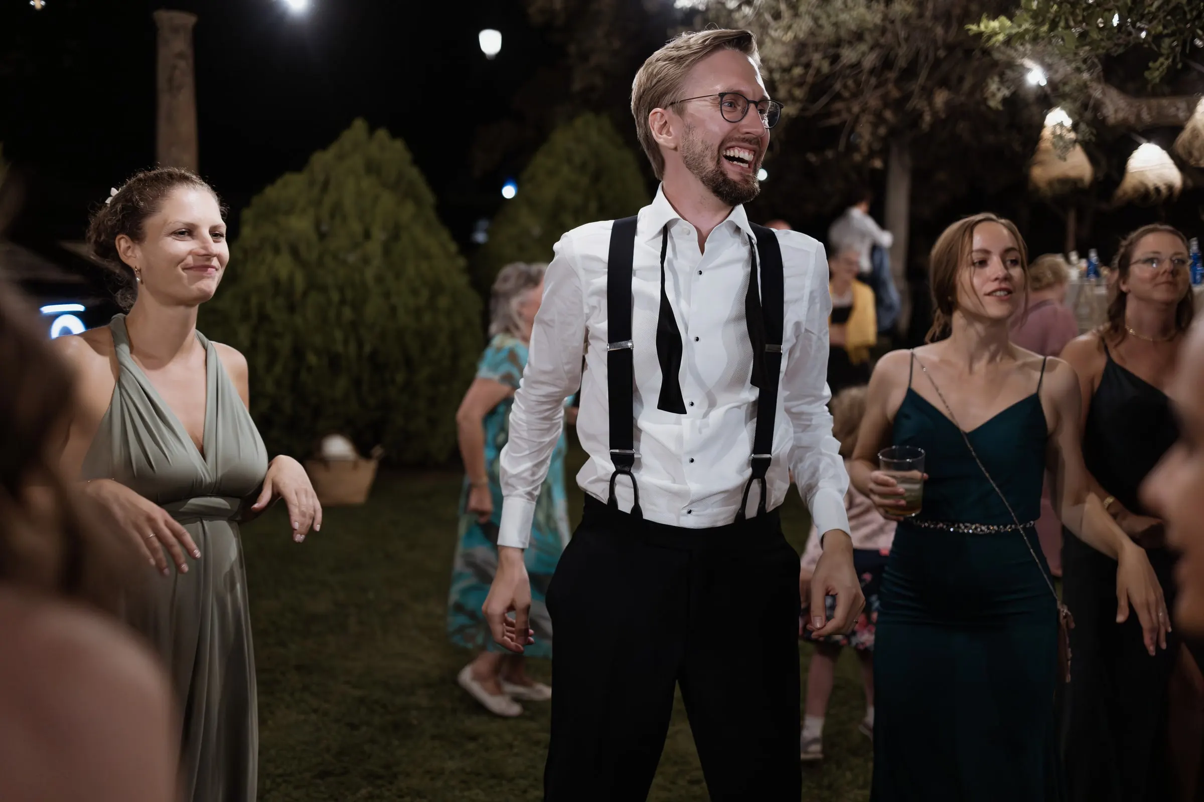 Groom dancing with friends under the cypresses at night in Ronda