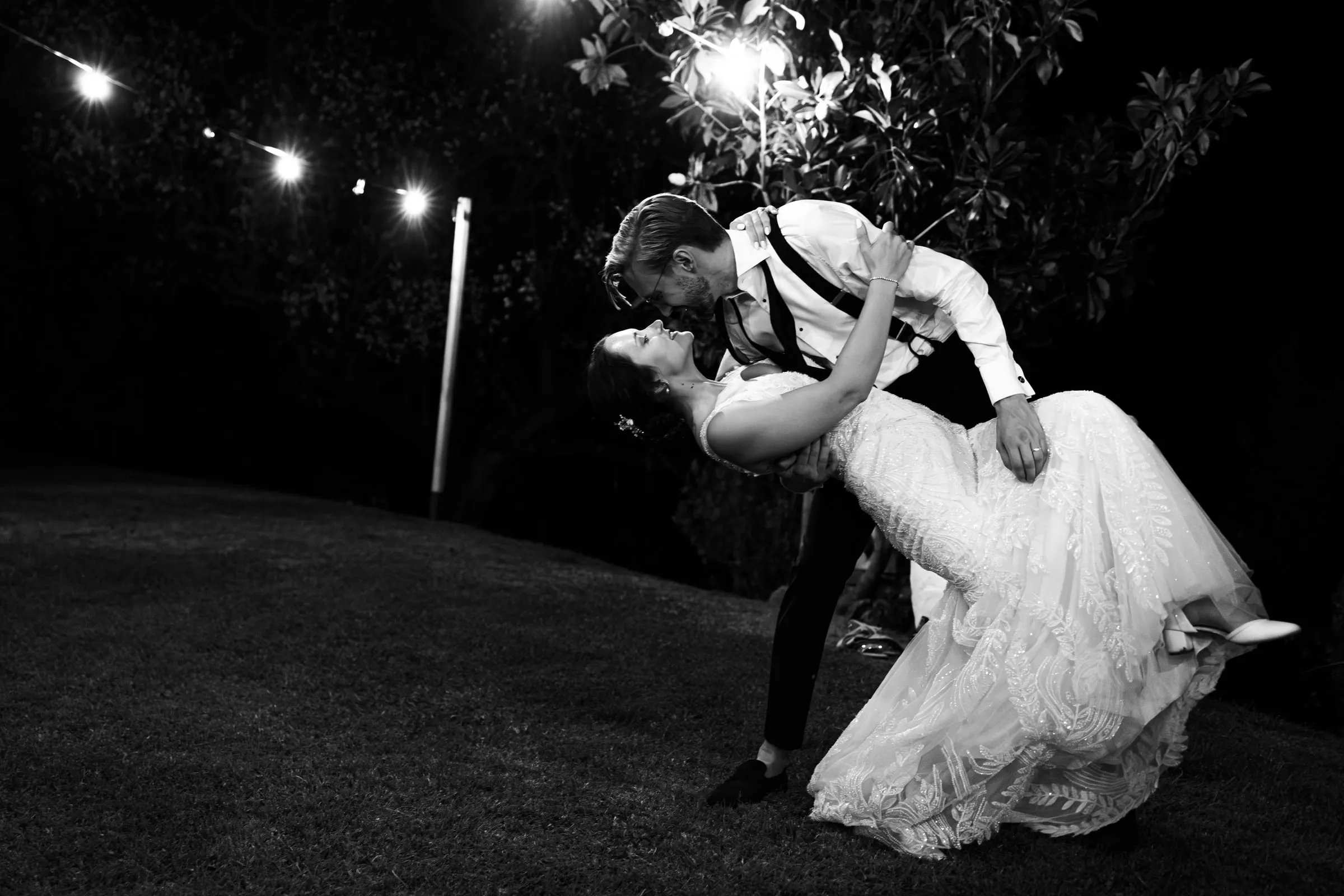 Black and white dip kiss under the string lights to end the night
