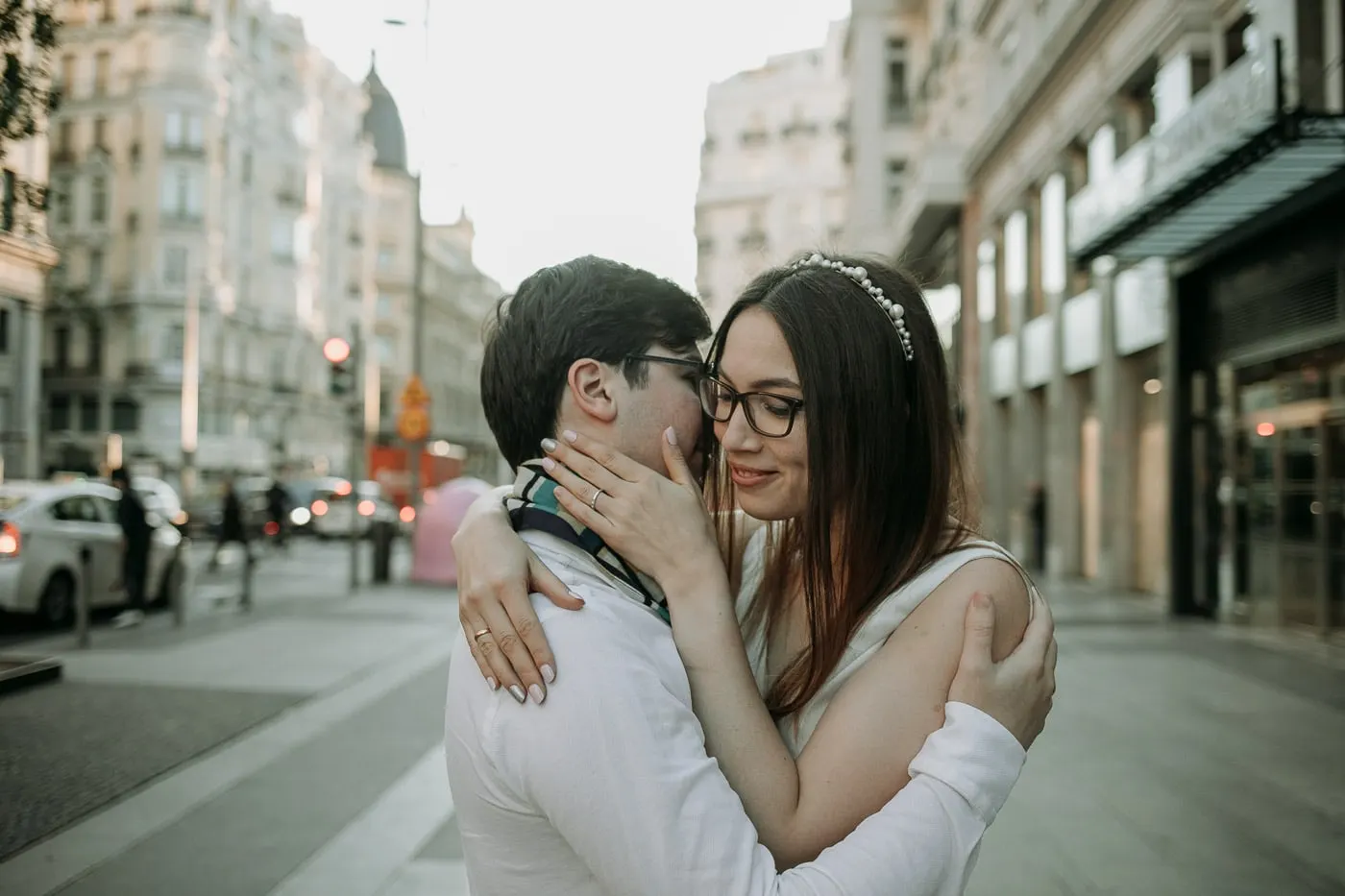 Bride in glasses kissing the groom's cheek on a Madrid pavement