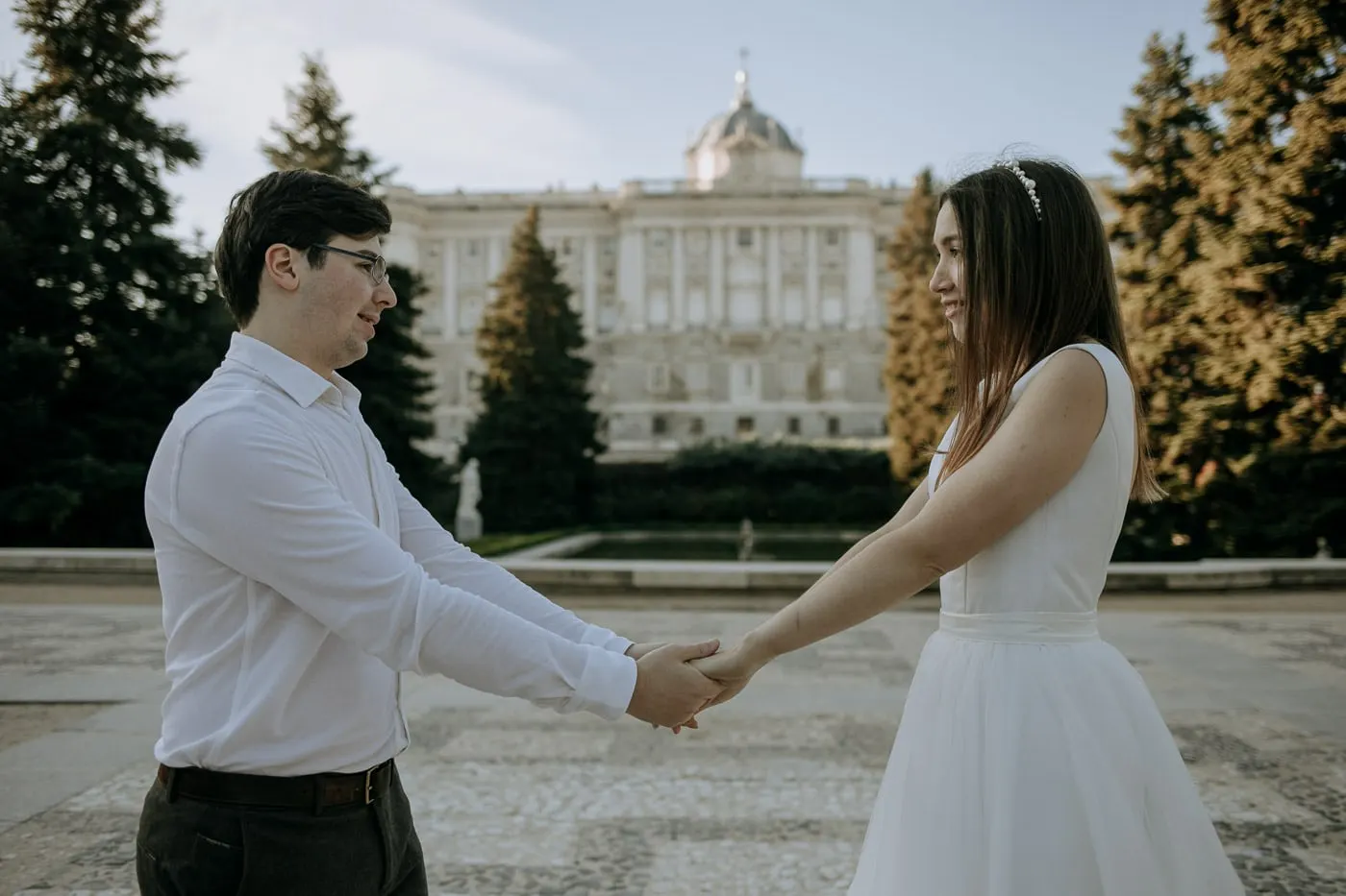 Couple reaching for each other's hands in Plaza de Oriente, the Royal Palace behind