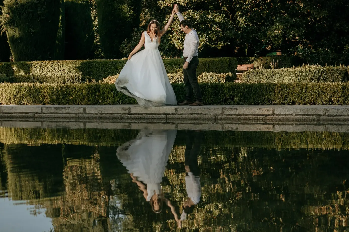 Bride twirling in her tulle skirt beside the pond, reflected below