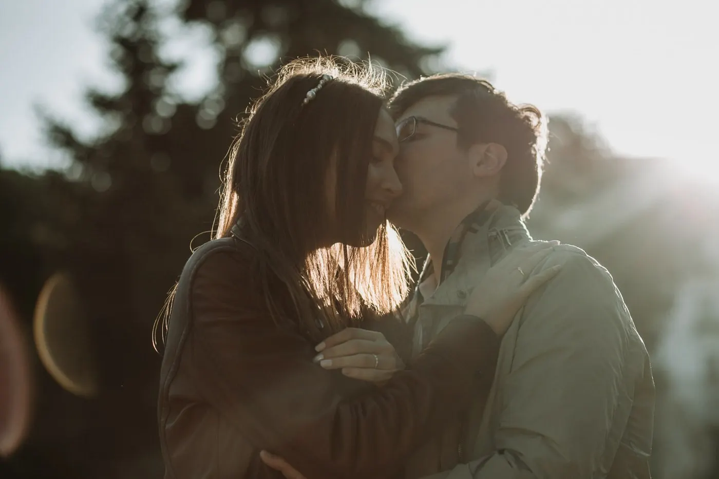 Groom kissing the bride's cheek with the sun behind them