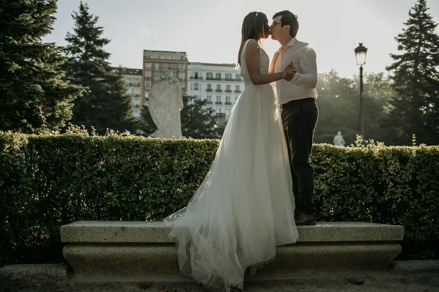 Bride standing on a stone bench to kiss the groom in the palace gardens