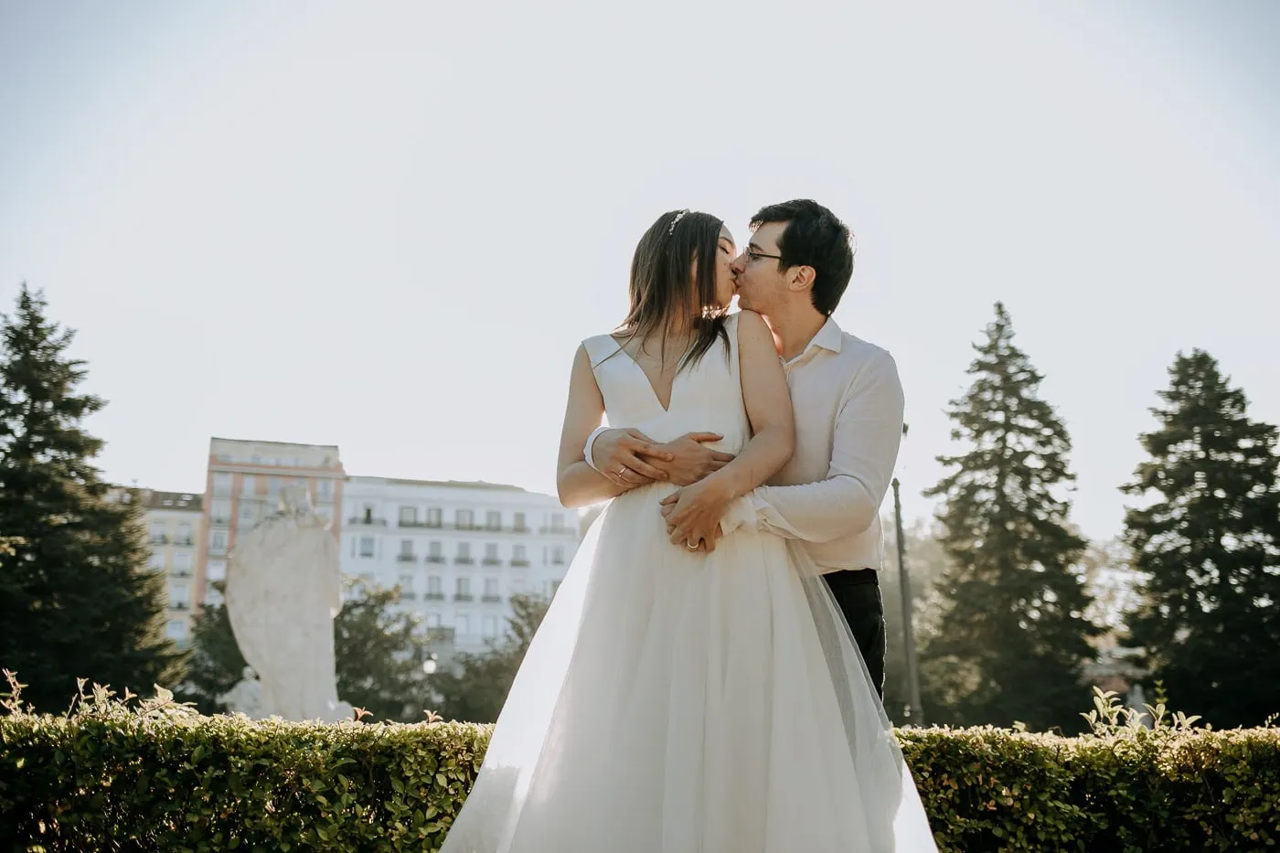 Couple kissing above a clipped hedge with apartment buildings behind