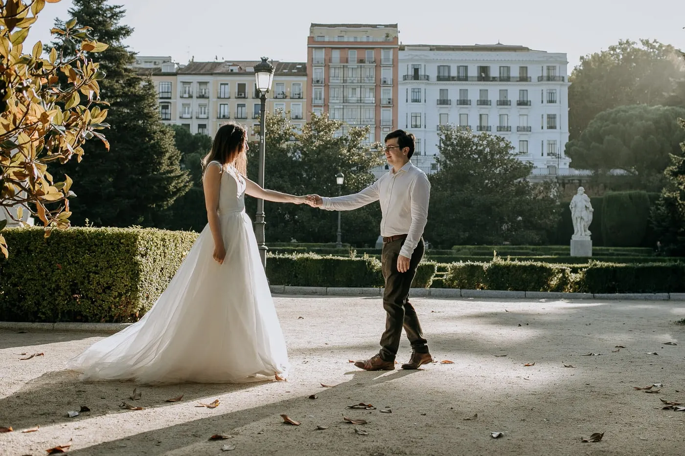 Bride and groom holding hands across a sunlit garden path, Madrid