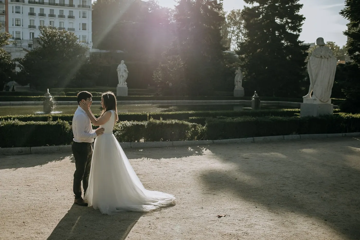 Couple embracing in a sunbeam among statues and parterres, Madrid