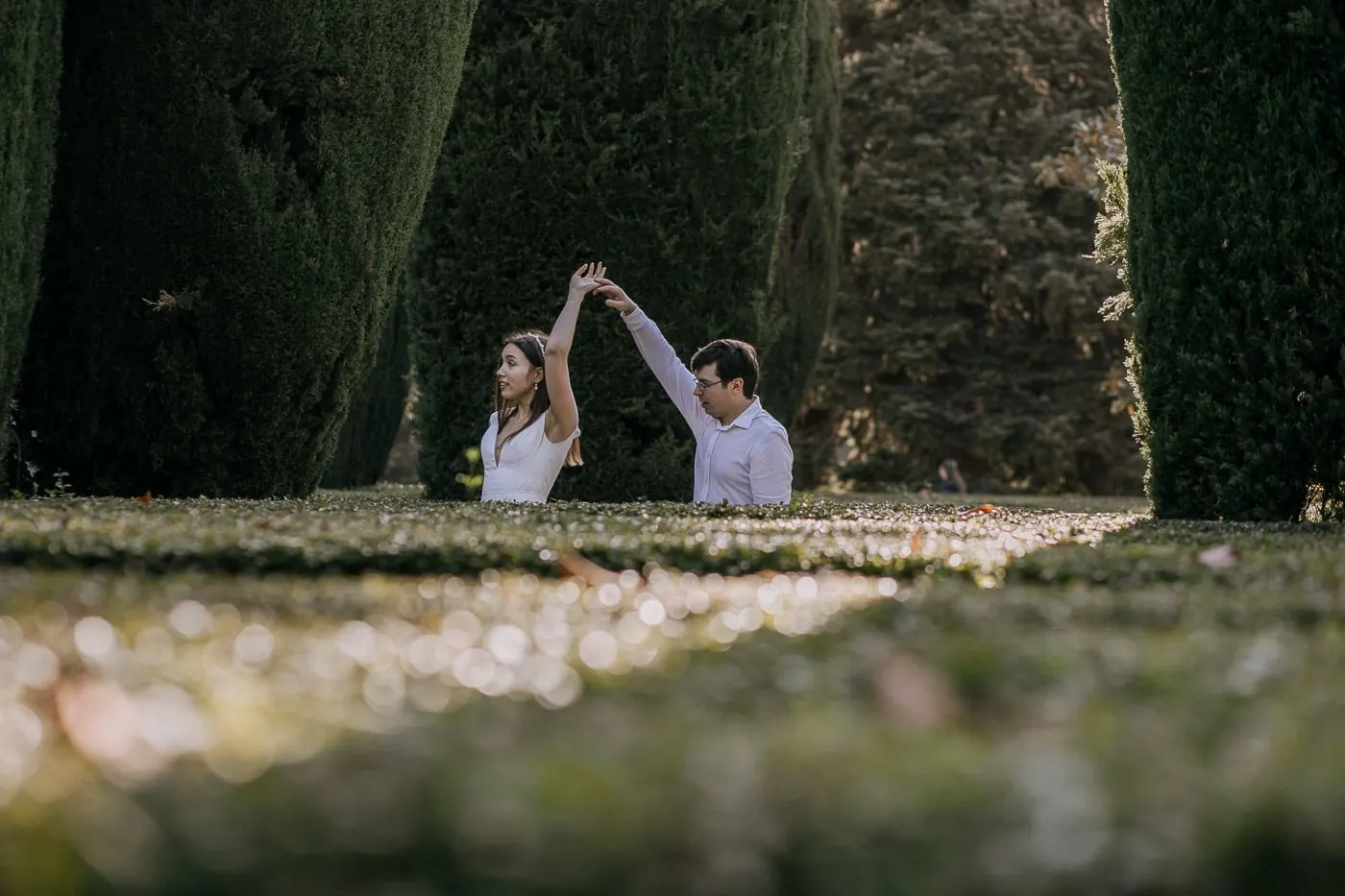 Groom twirling the bride between tall clipped cypress hedges