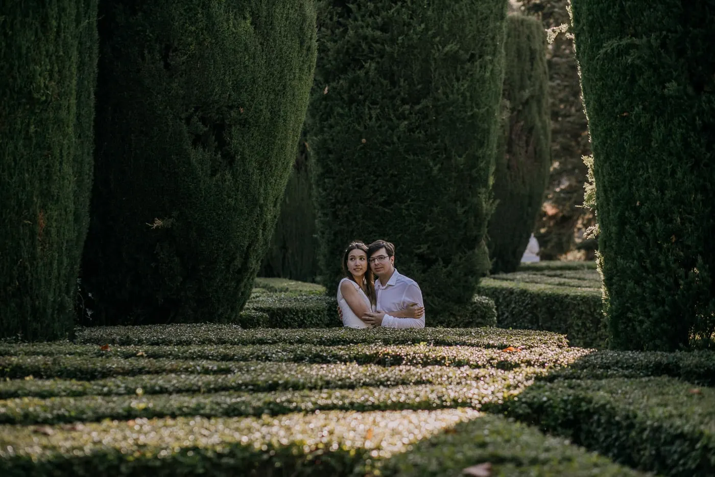 Couple peeking out from the low hedges of the formal garden