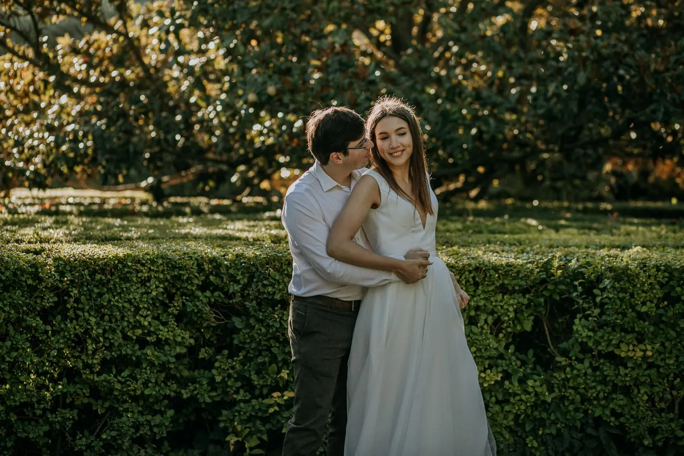 Groom kissing the bride's cheek beside a hedge, Madrid