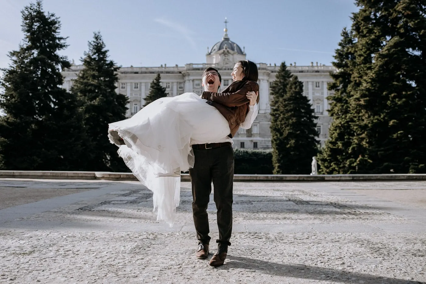 Groom carrying the bride and laughing in front of the Royal Palace, Madrid