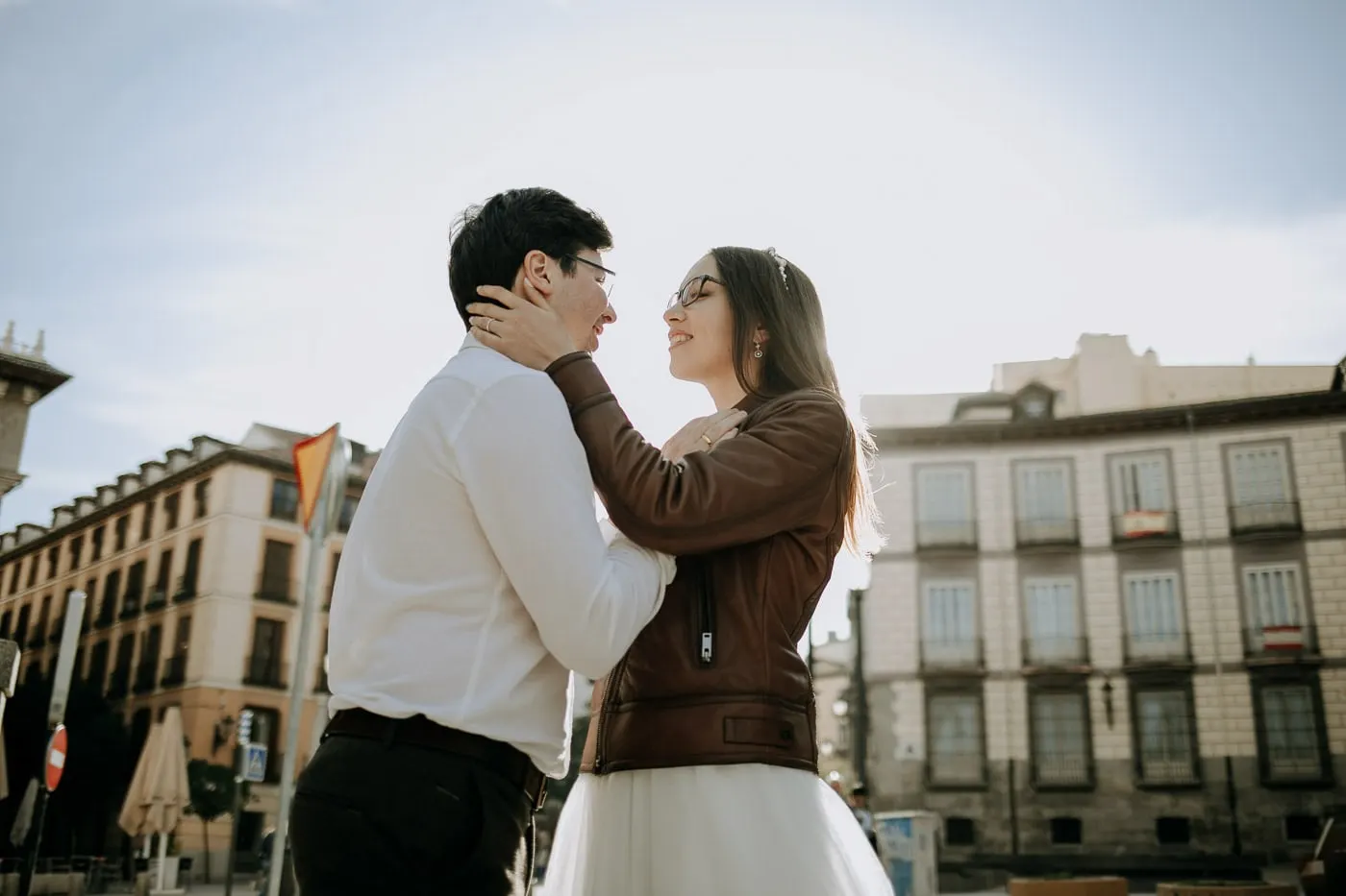 Groom holding the bride's face against a bright sky, old Madrid buildings behind