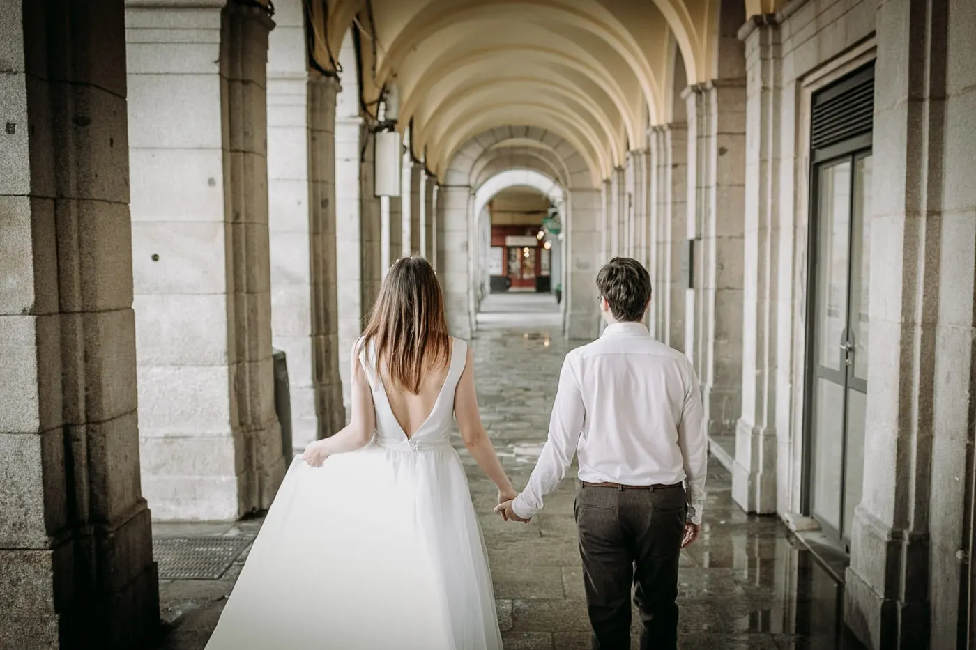 Couple walking hand in hand under the arcades of Plaza Mayor, Madrid