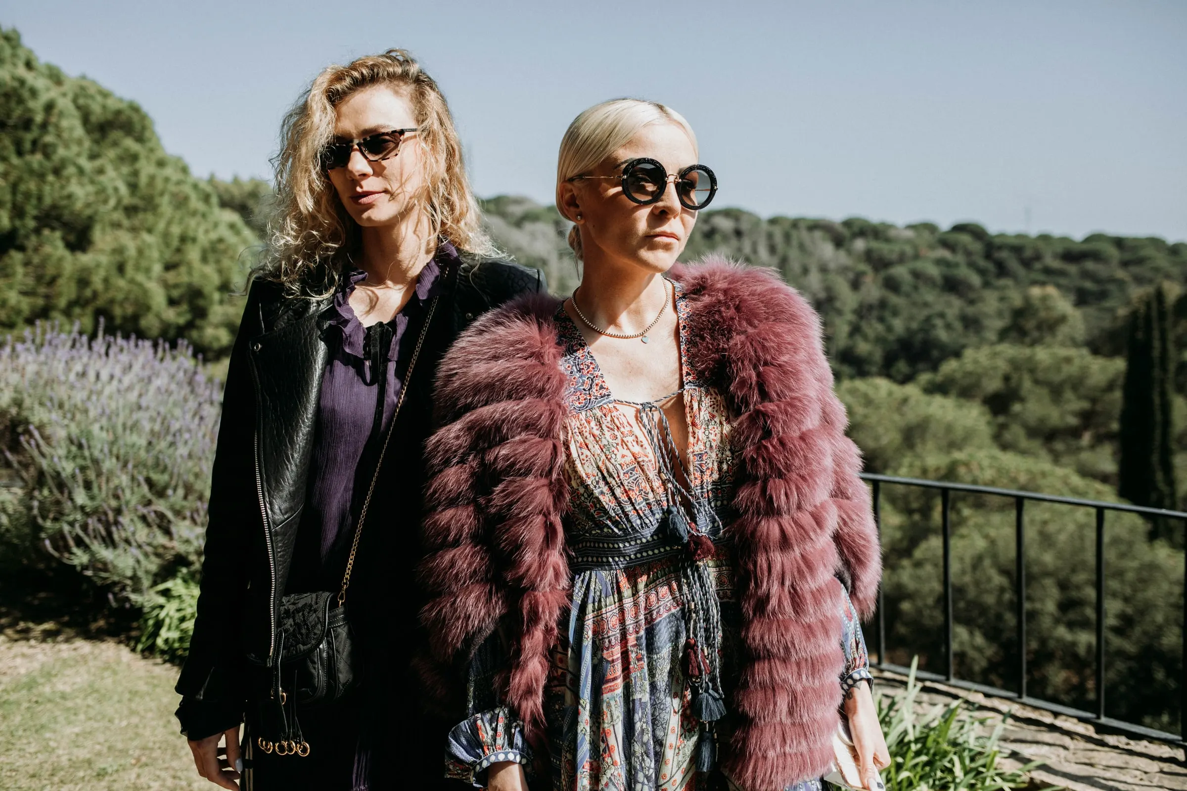 Two guests in sunglasses, one in a burgundy fur jacket, on the hillside terrace of a masia in Girona