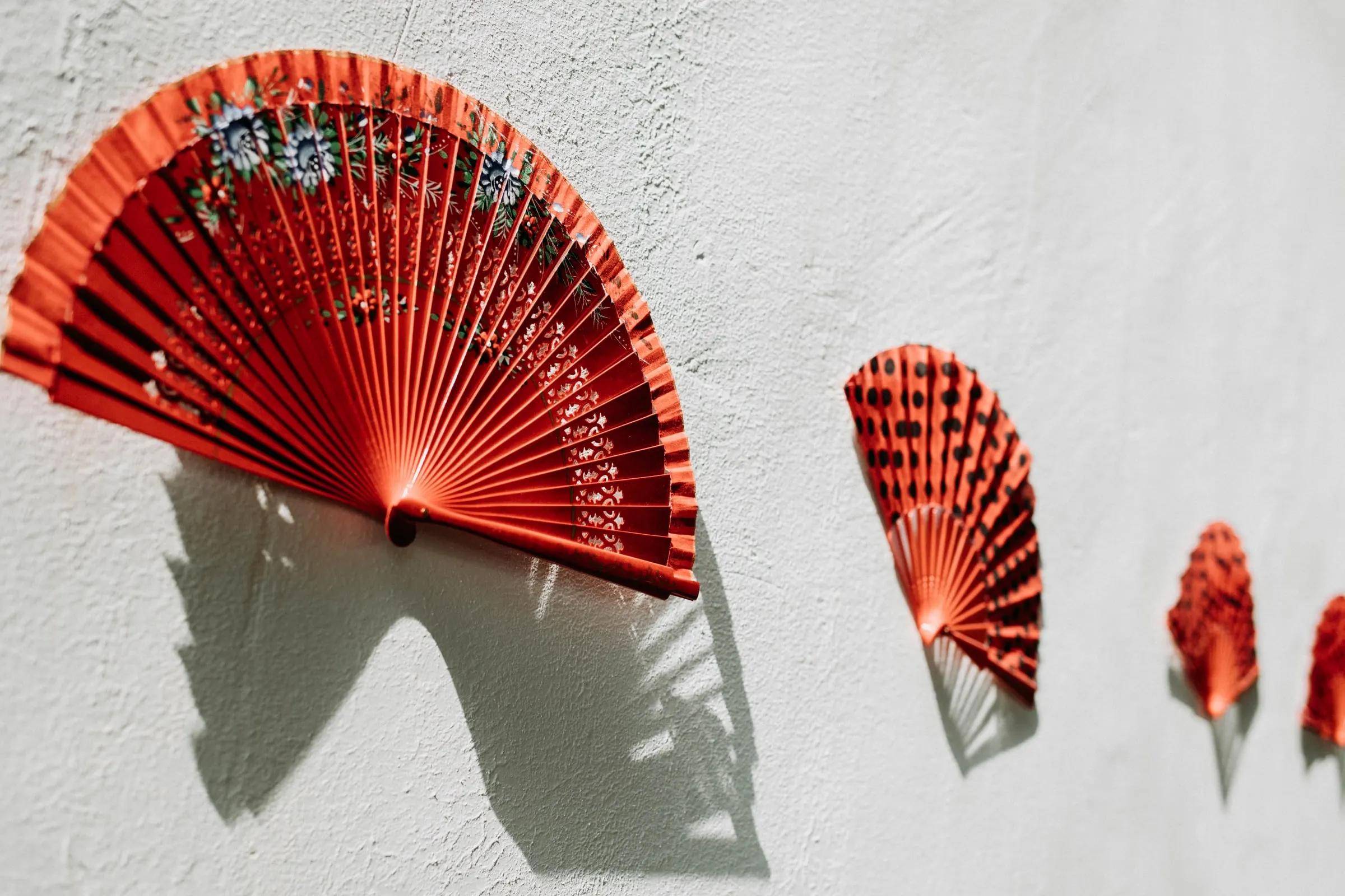 Red Spanish fans hung on a whitewashed wall, casting sharp shadows, at a masia in Girona