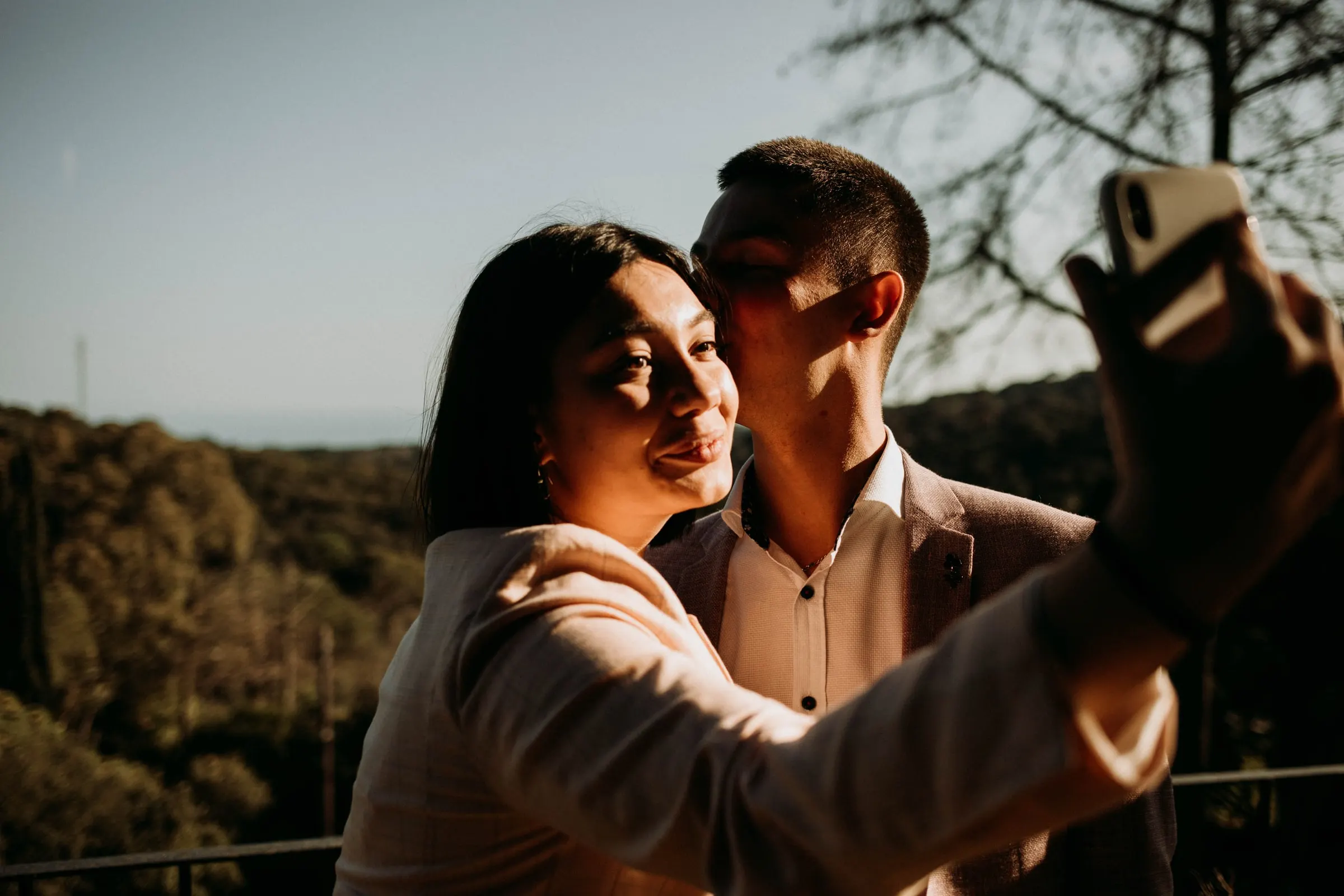 Two guests taking a selfie at sunset against the wooded hills of a masia in Girona