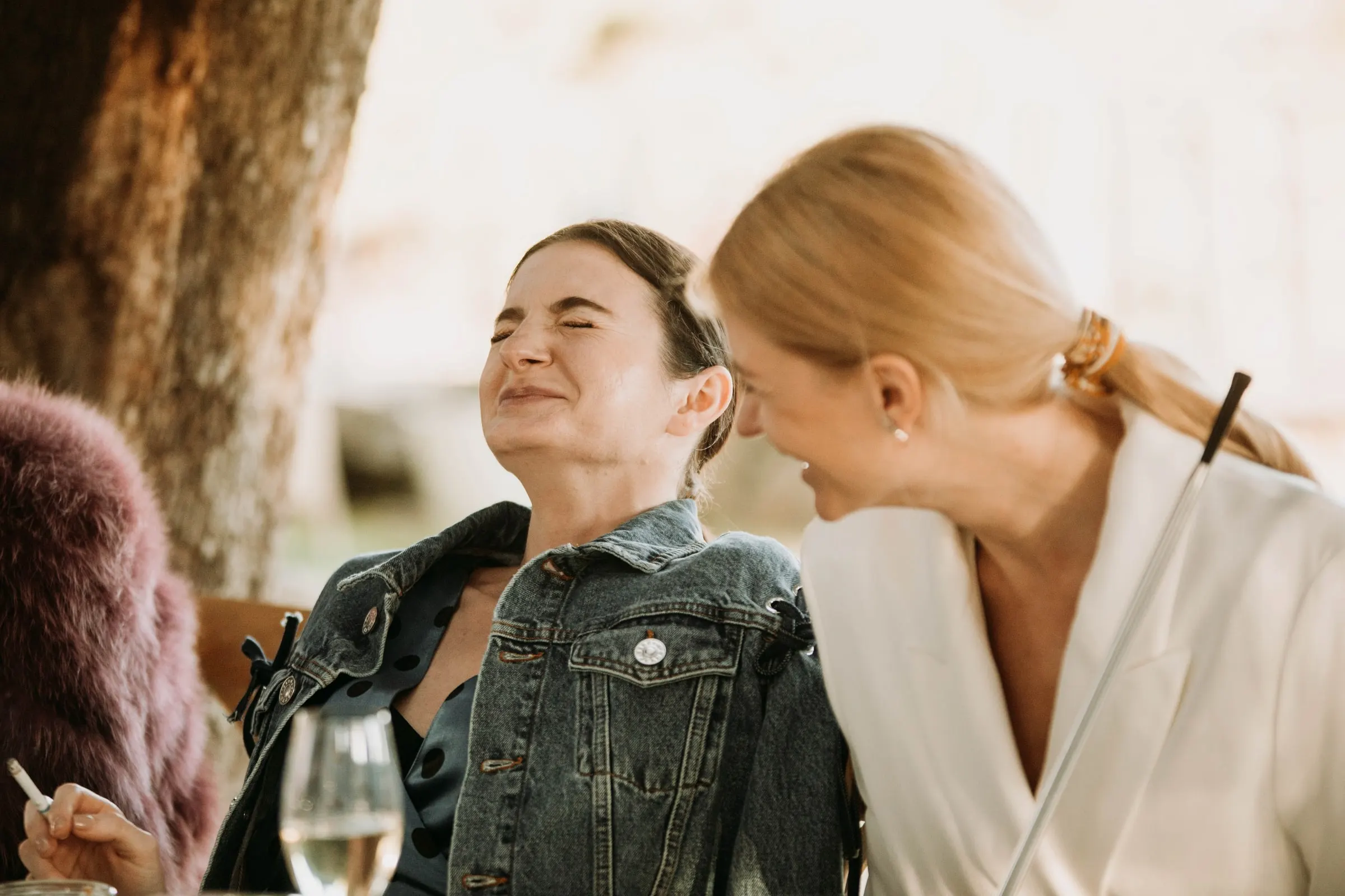 The bride laughing with a friend in a denim jacket during the drinks at a masia in Girona