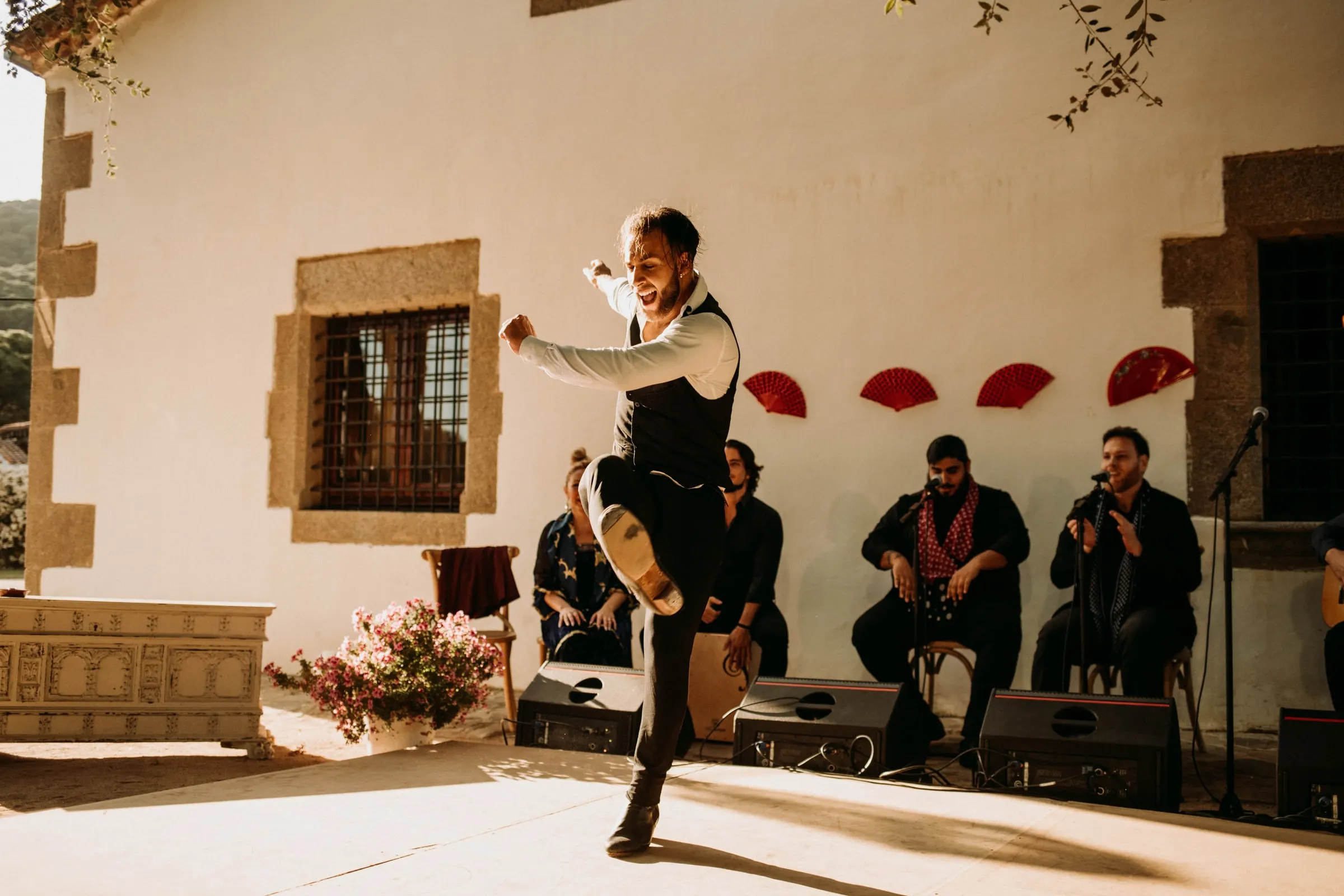 A flamenco dancer leaping in front of the musicians and red fans on the patio of a masia in Girona