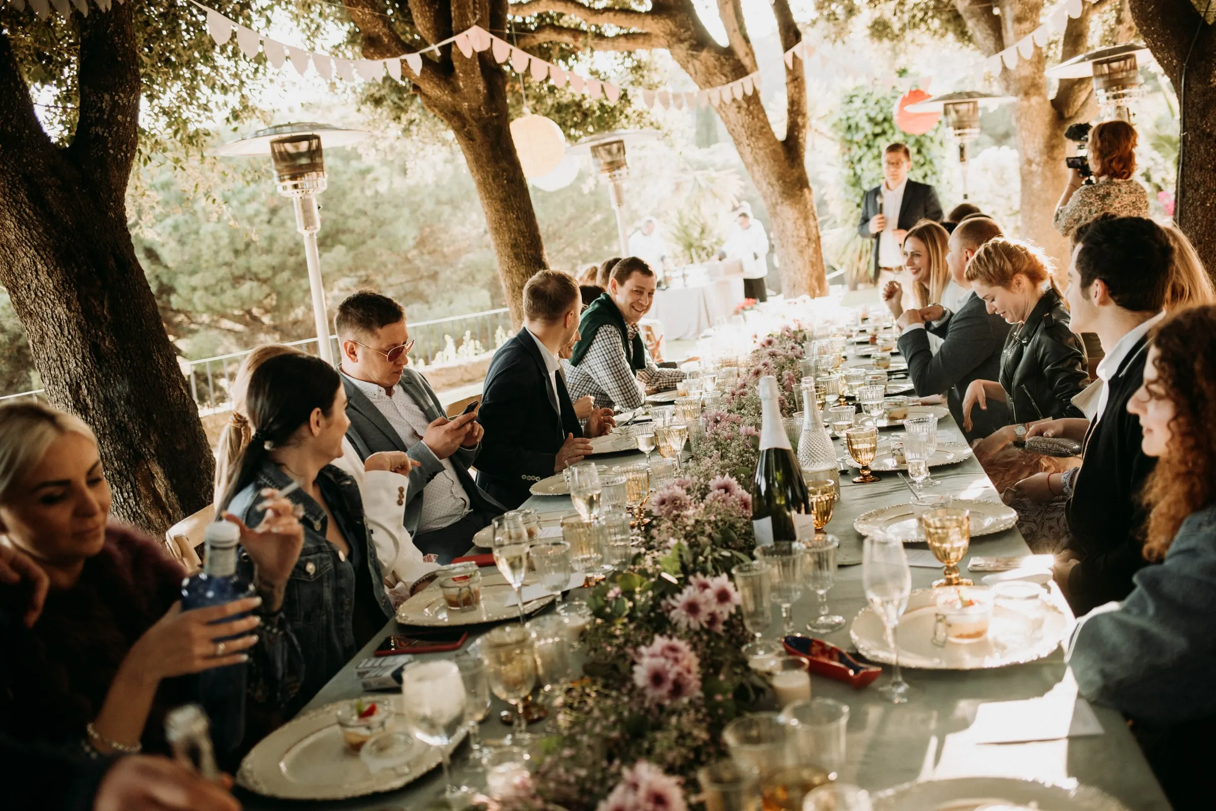 Guests chatting along the long table under the trees during lunch at a masia in Girona