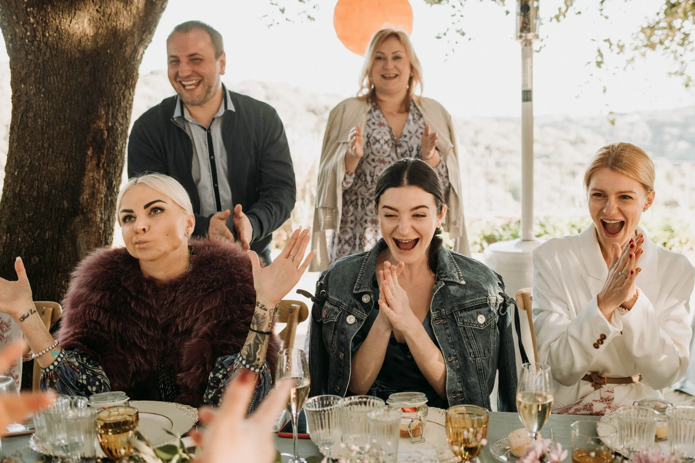 Guests at the table cheering and clapping, the bride smiling among them, at a masia in Girona