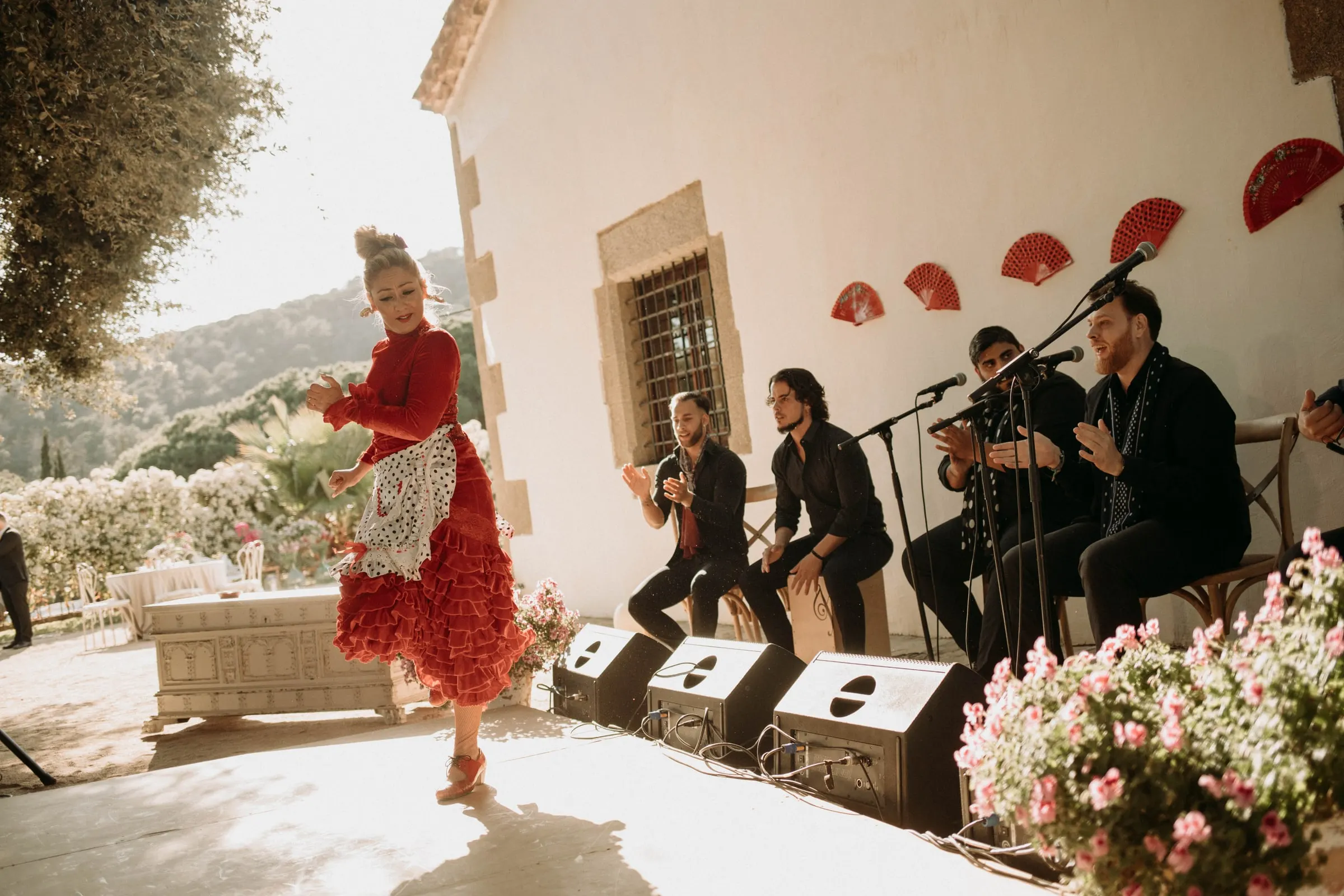 A flamenco dancer in a red ruffled dress performing with the band on the patio of a masia in Girona