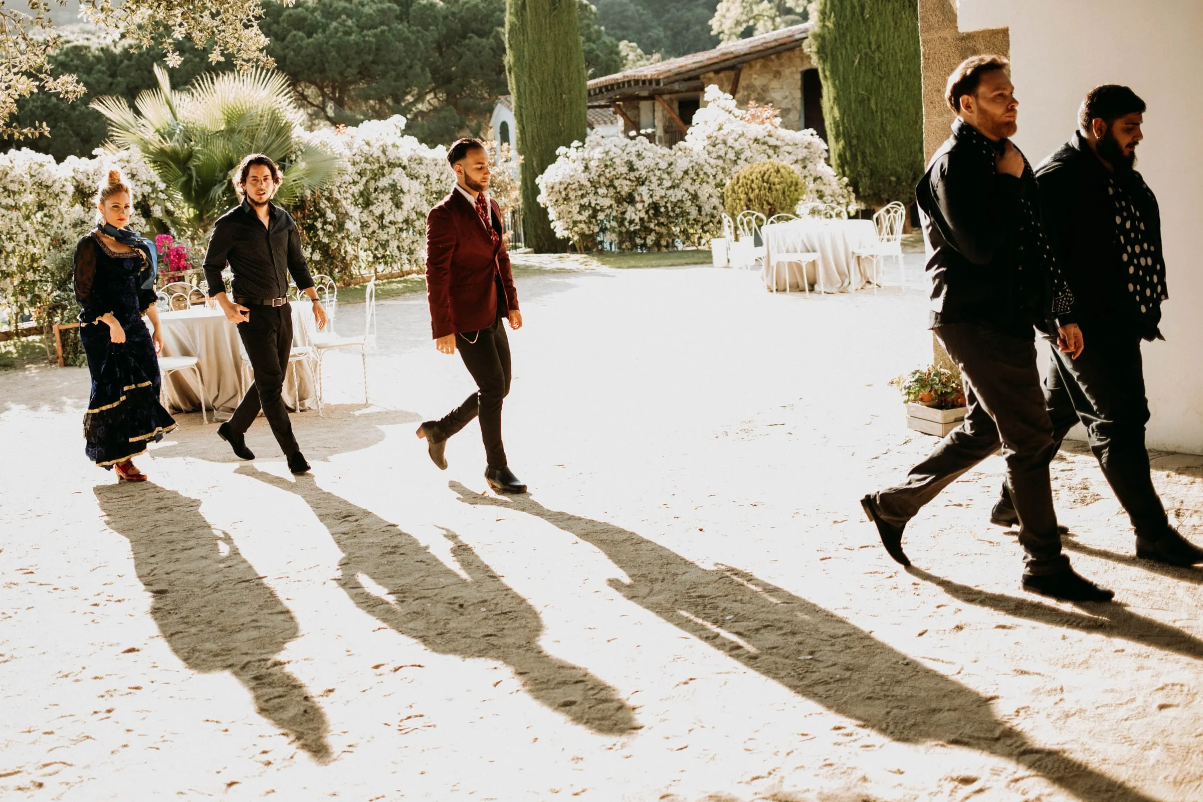The flamenco musicians and dancers walking across the sunny courtyard of a masia in Girona