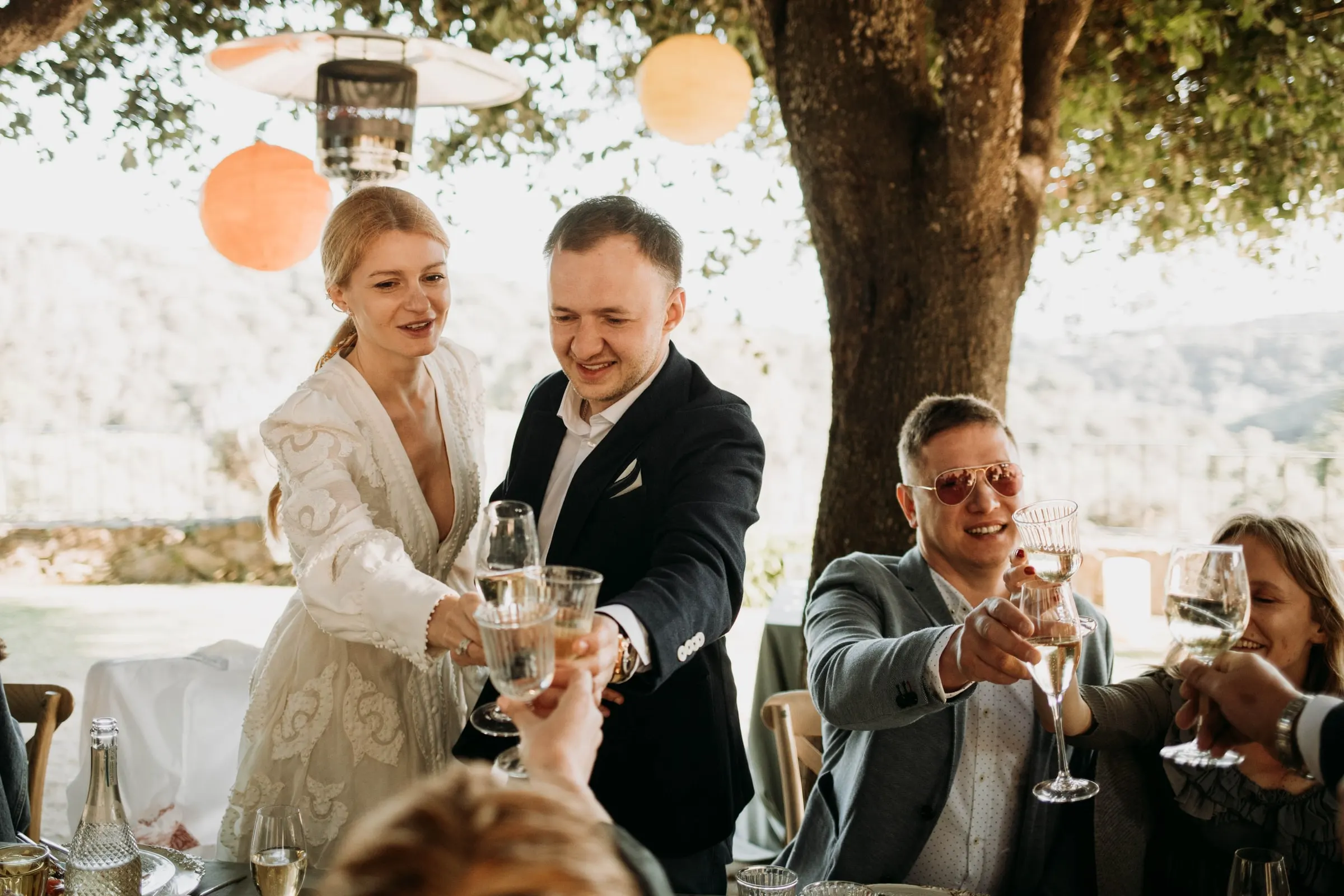 Bride and groom clinking glasses with guests standing round the table at a masia in Girona