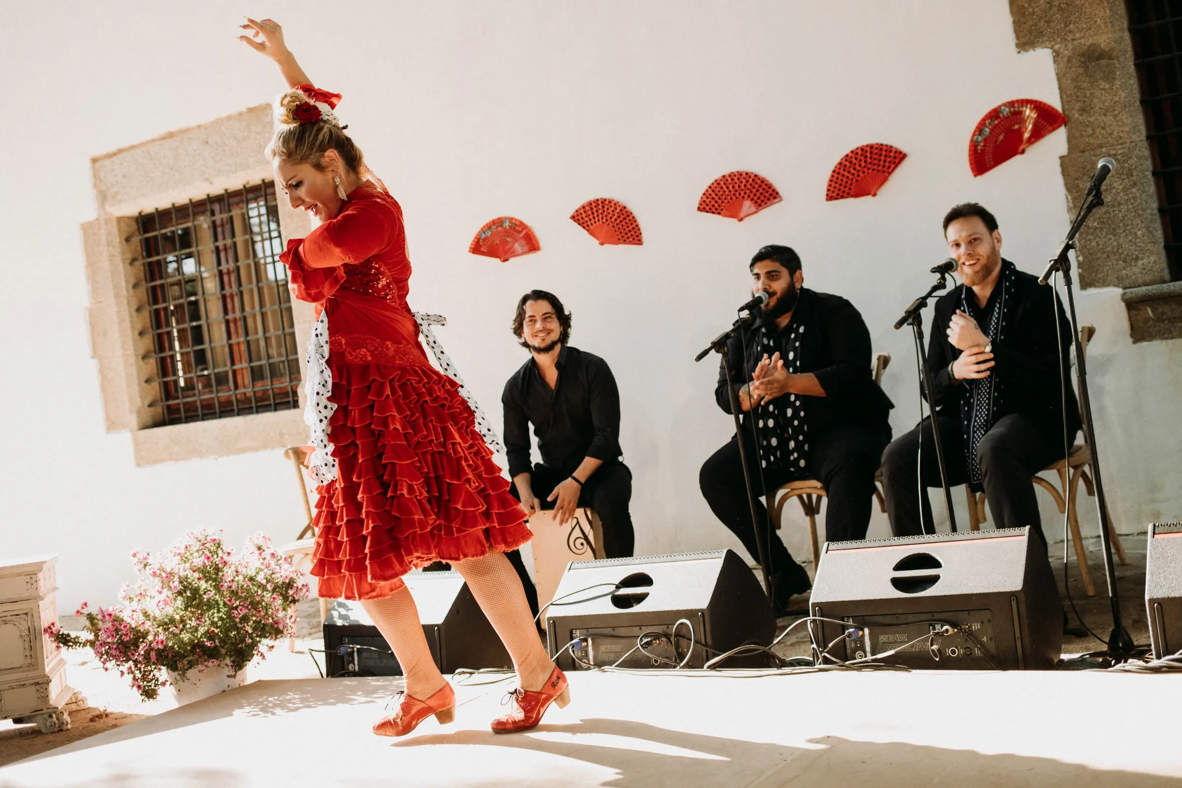 A flamenco dancer in red with her arm raised, the band playing behind, at a masia in Girona