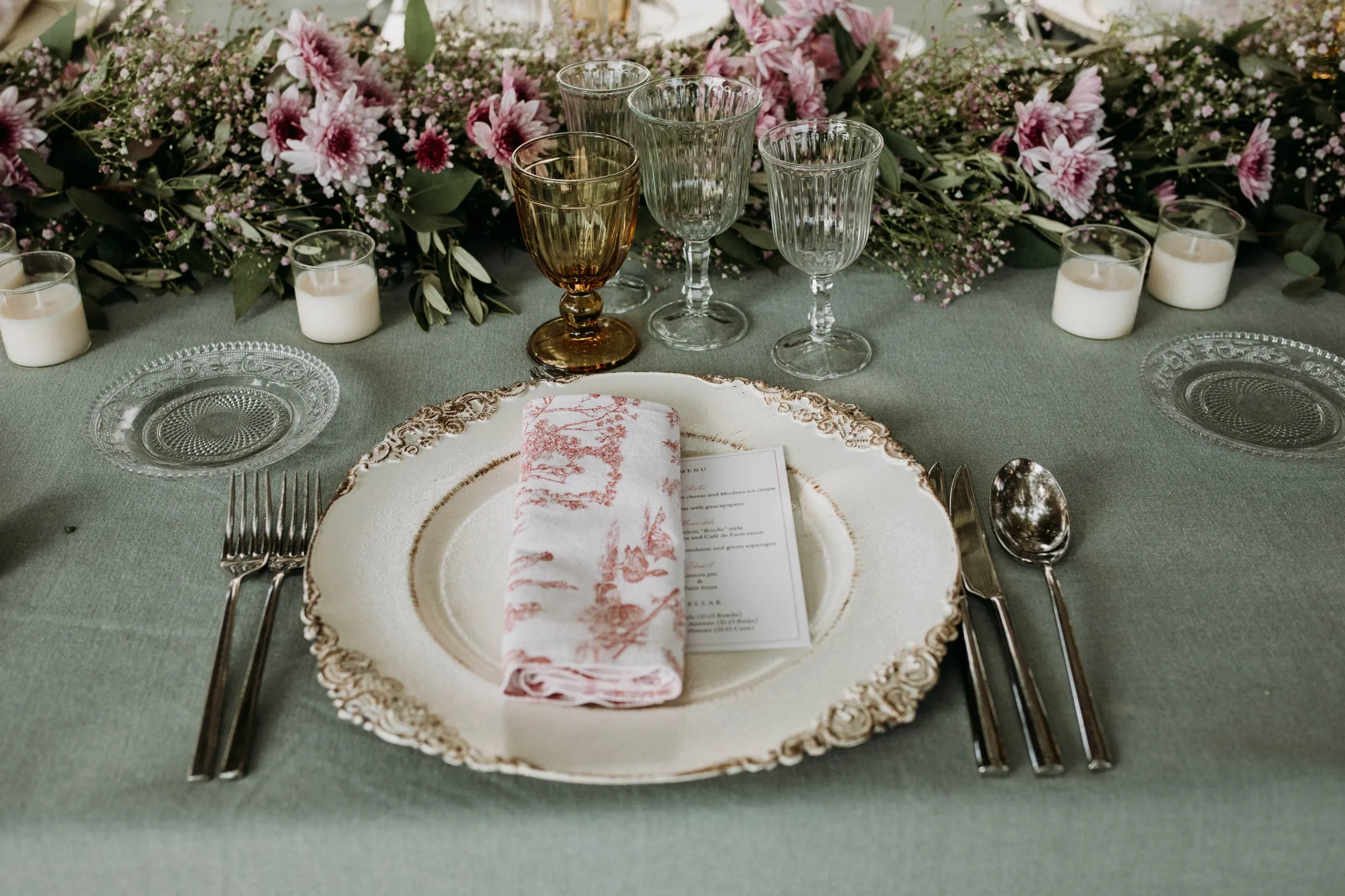 A place setting with a toile napkin, gold-rimmed plate and amber glass at a masia in Girona