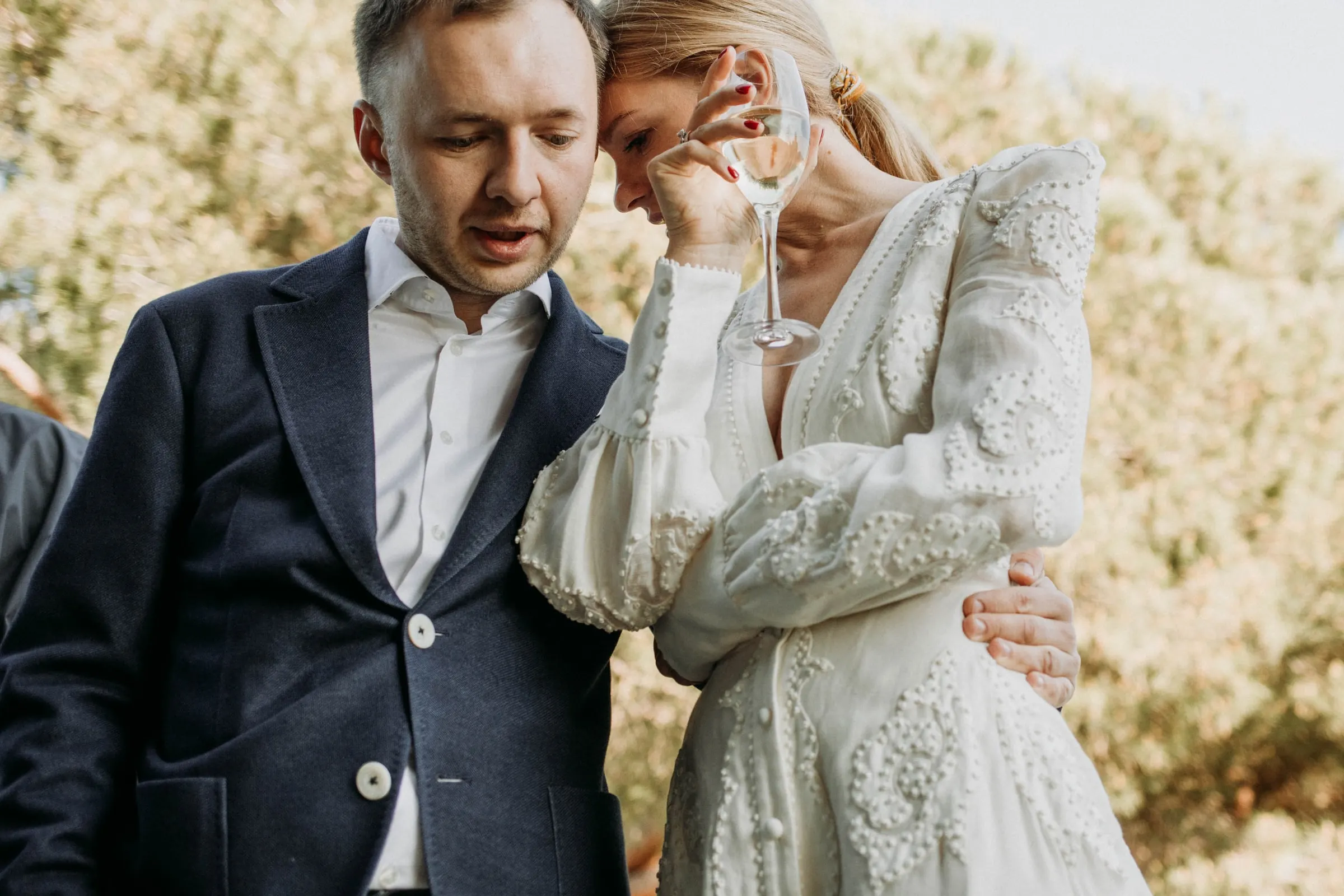 The groom holding the bride close as she leans on him with a glass of cava, at a masia in Girona