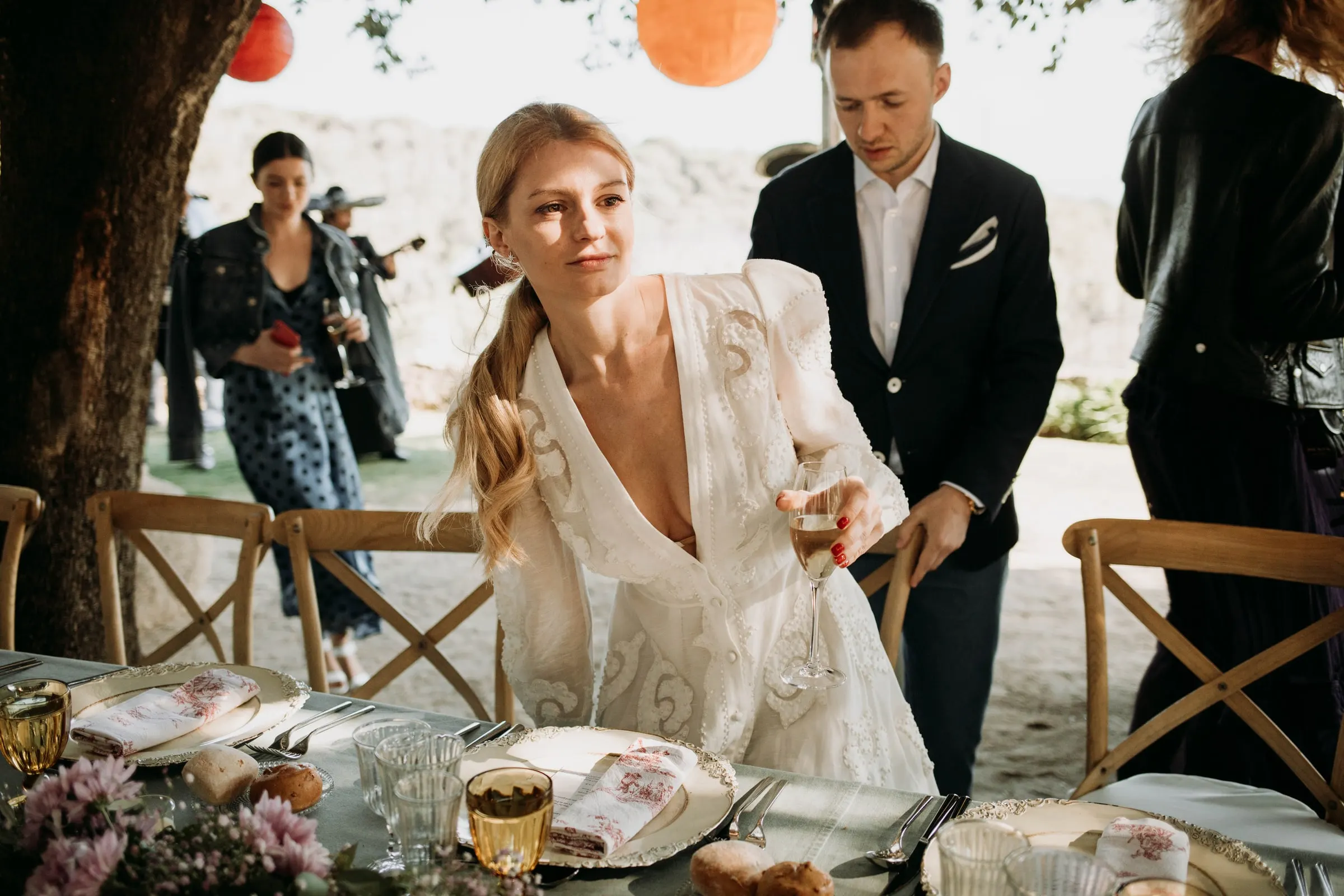 The bride sitting down at the banquet table as the groom pulls out his chair, at a masia in Girona