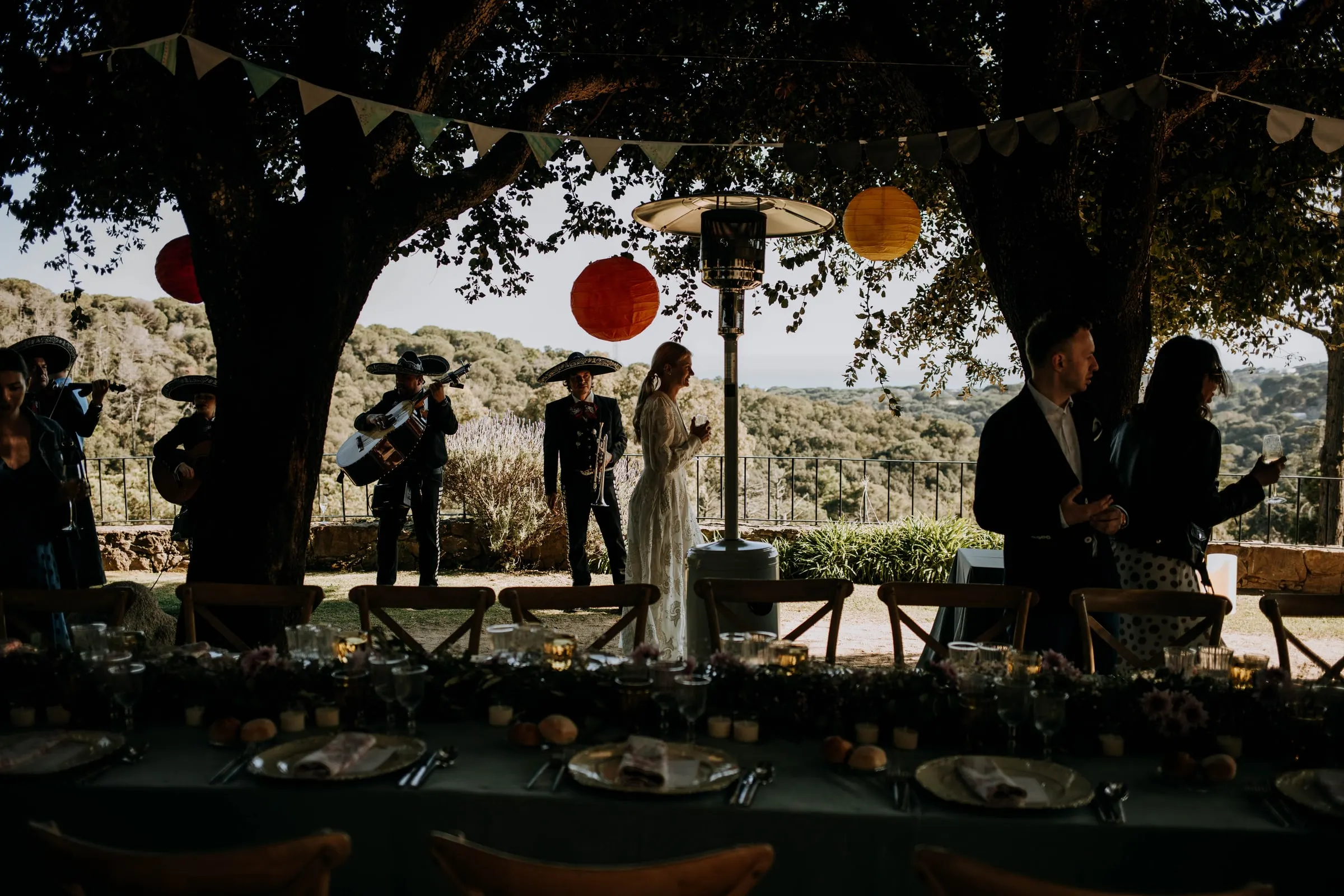 Mariachis serenading the couple at the end of the long table under the trees, at a masia in Girona