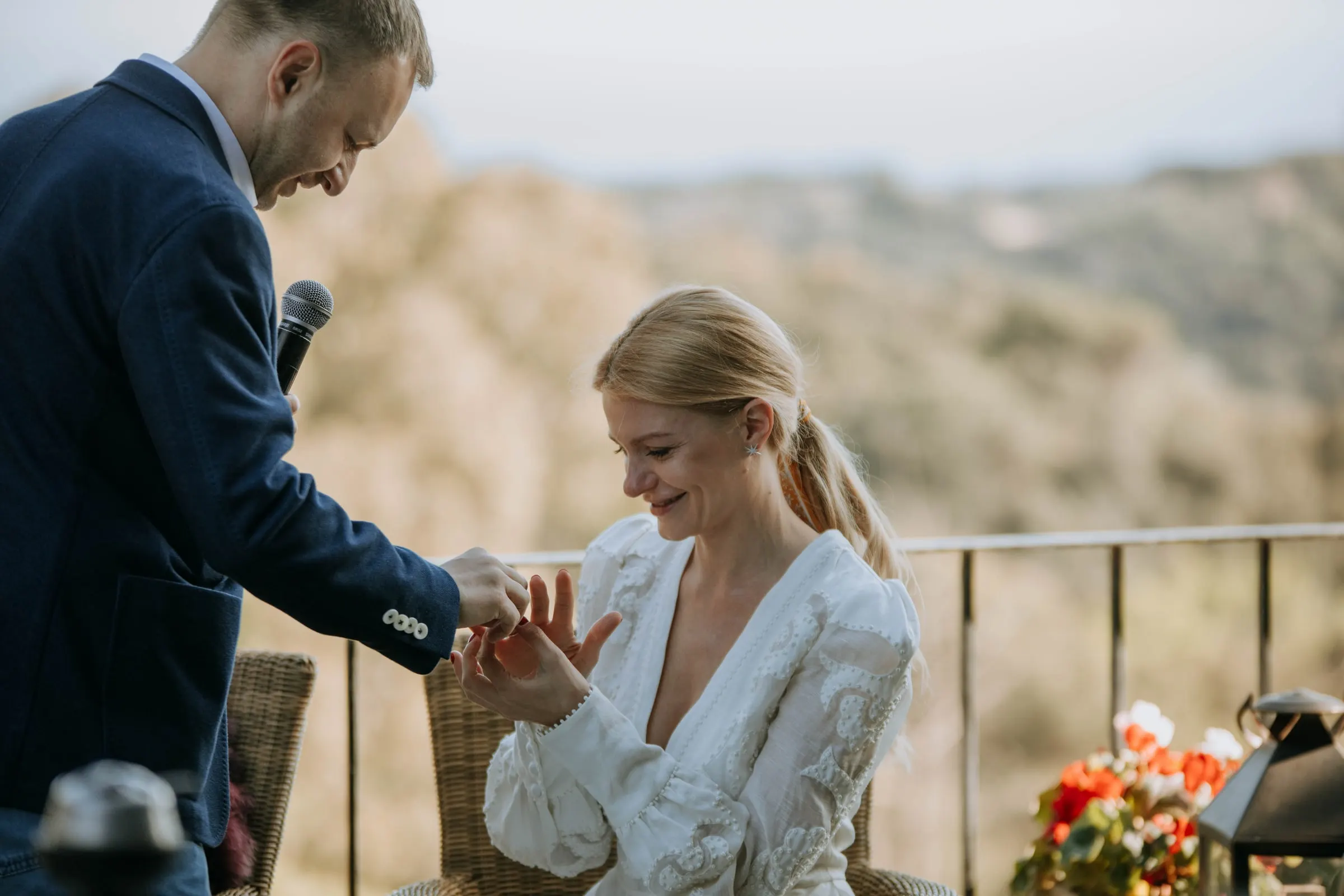 The groom kneeling to slip a ring on the seated bride's finger on the terrace of a masia in Girona