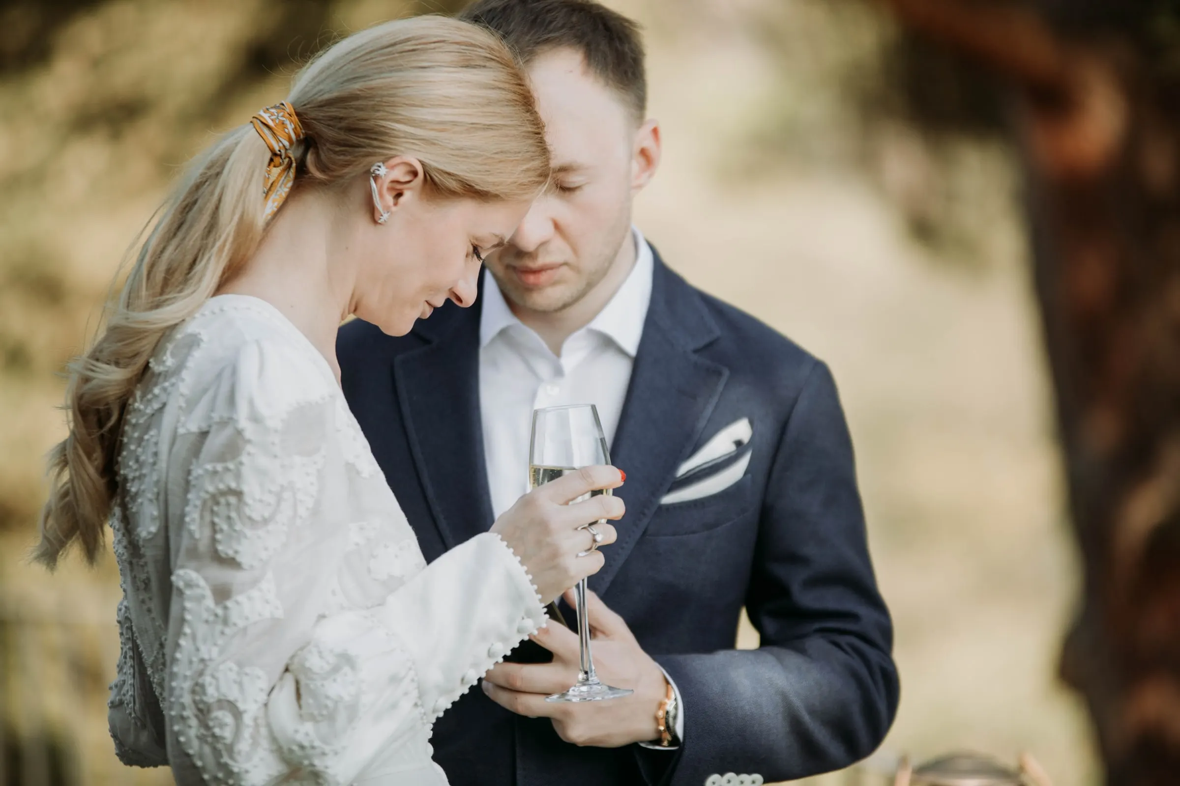 The groom resting his head against the bride's as she holds a glass, at a masia in Girona