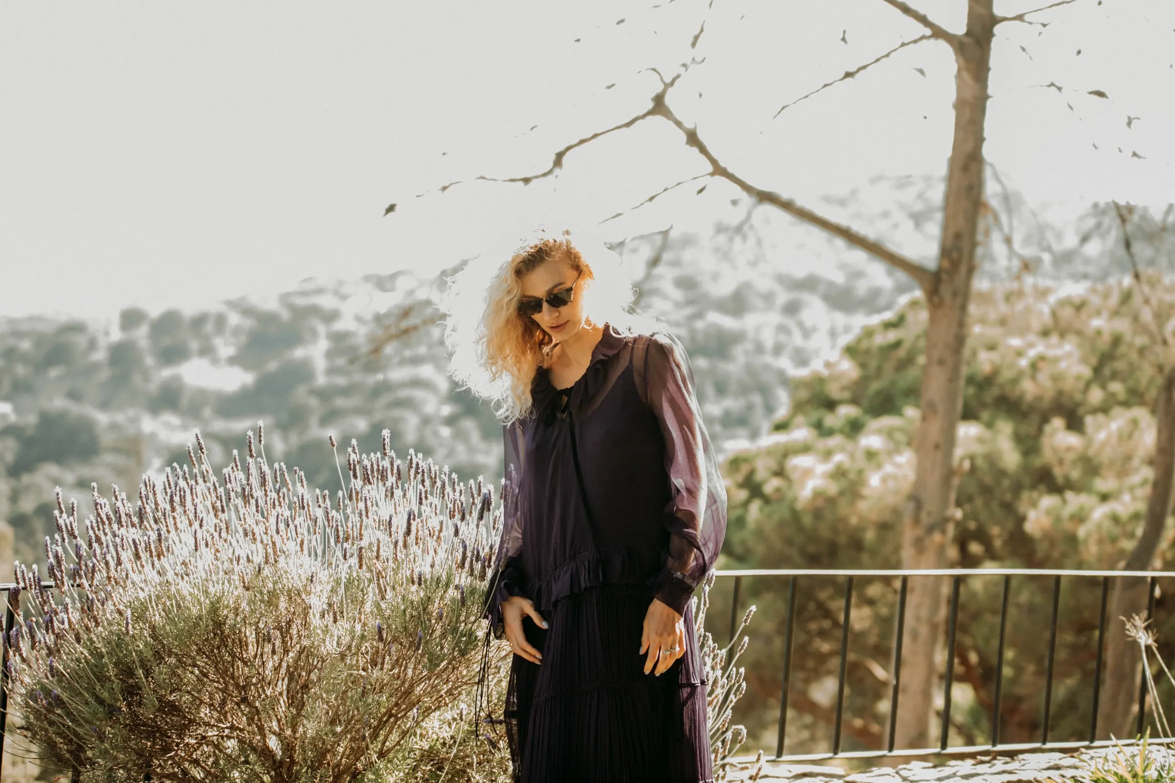 A guest in a purple dress and sunglasses walking past lavender at a masia in Girona