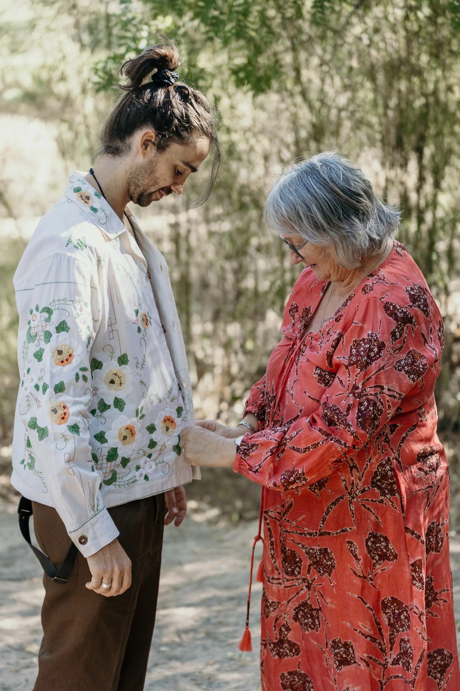 Groom's mother in a red floral dress holding his hands before the wedding
