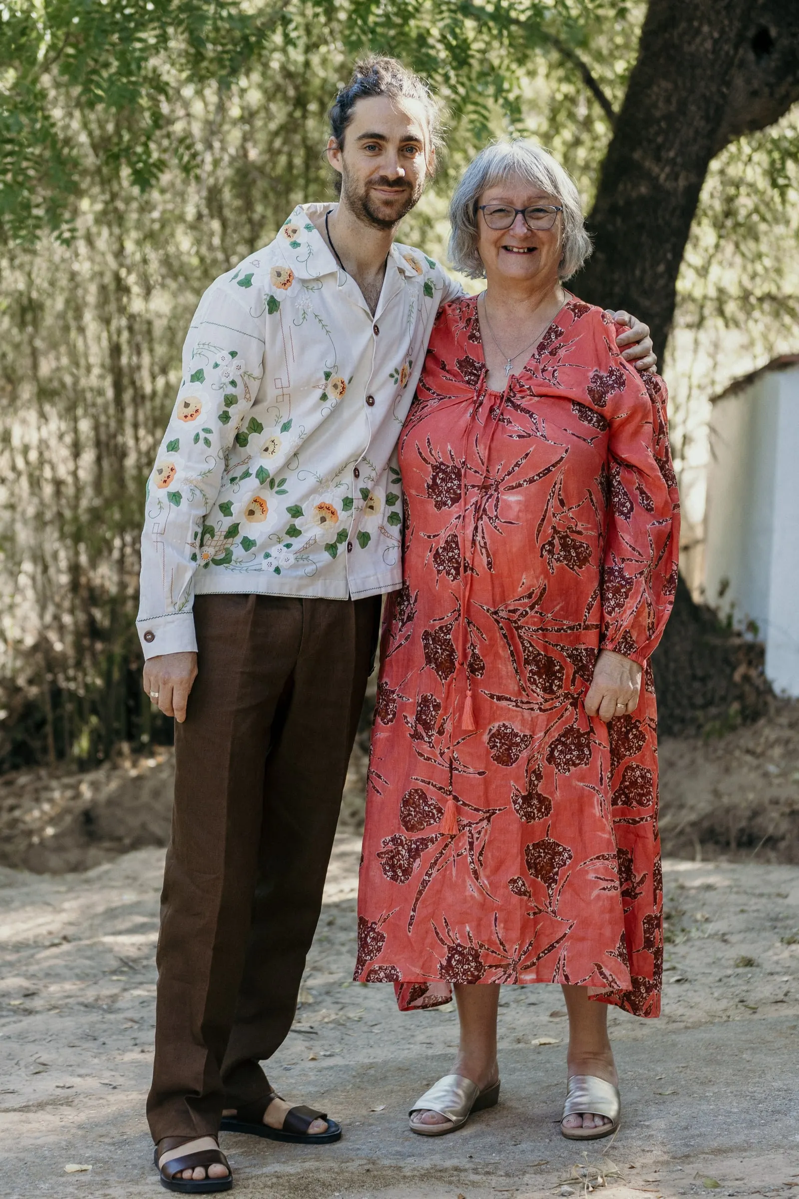 Groom in an embroidered flower shirt posing with his mother in the shade