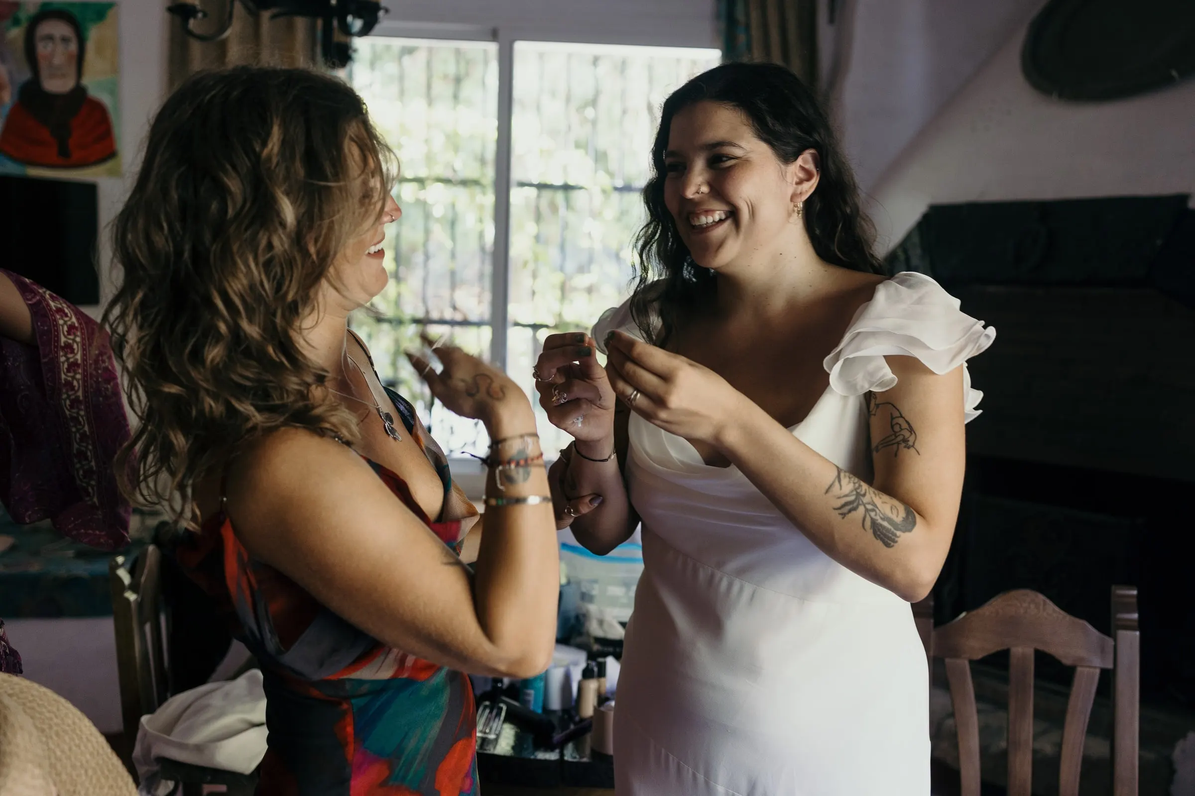 Bride laughing with a friend in a patterned dress while getting ready