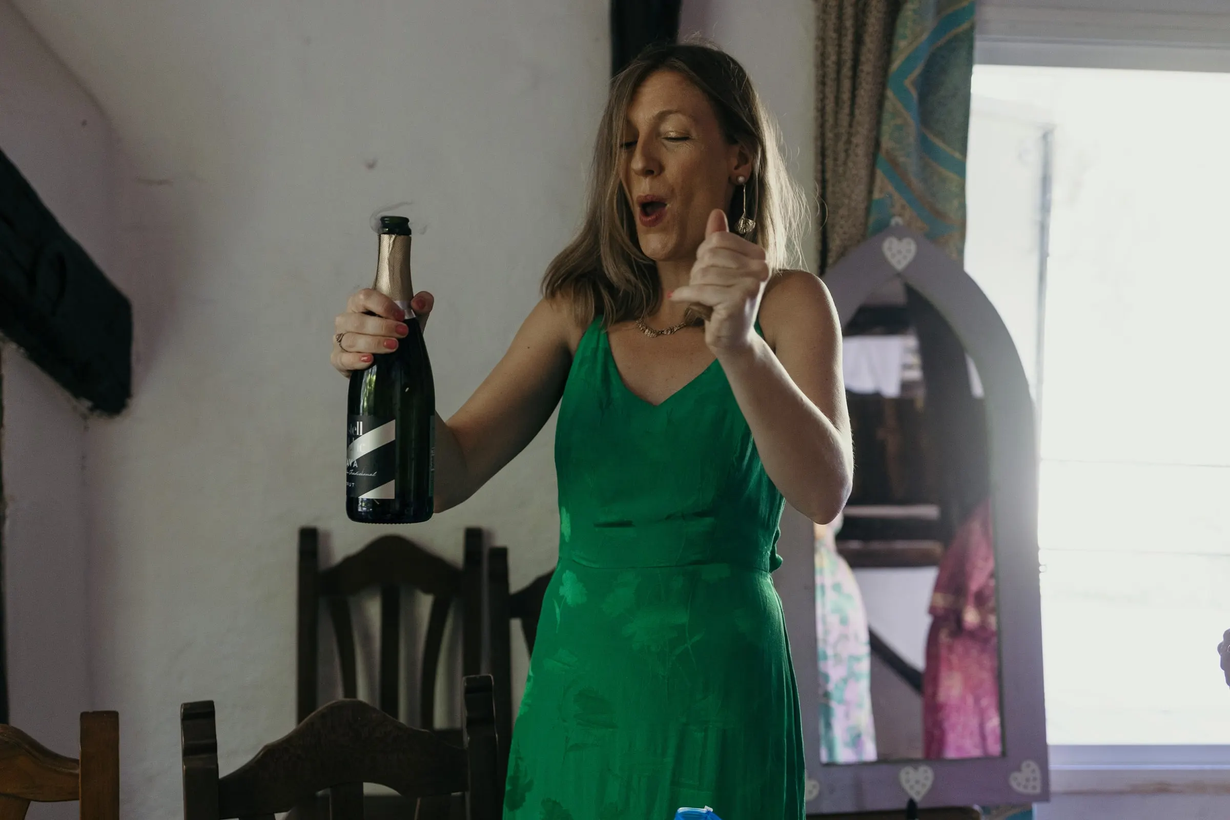 Friend in a green dress opening a bottle of cava in the bridal room