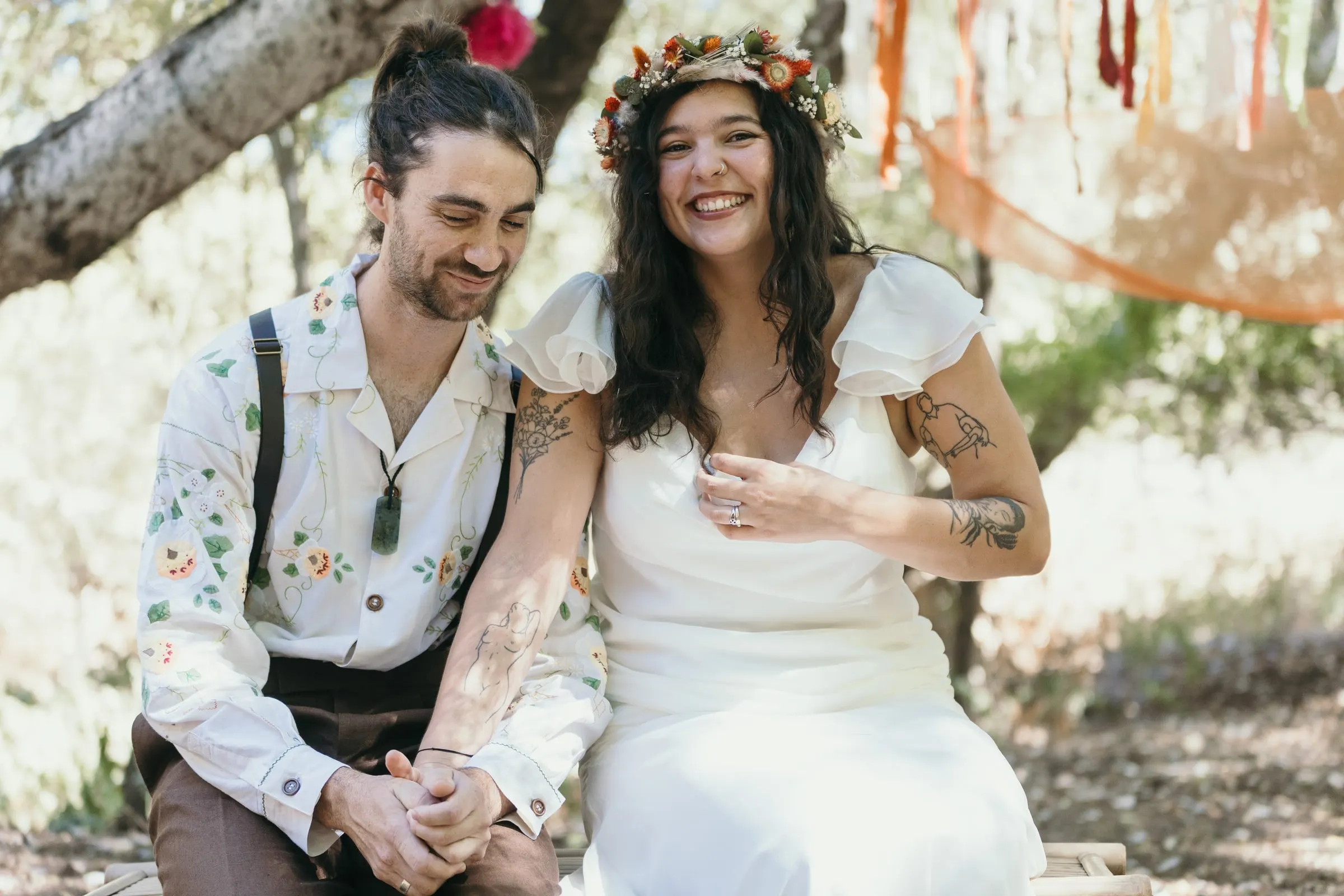 Bride and groom laughing on a bench under an old tree during the ceremony