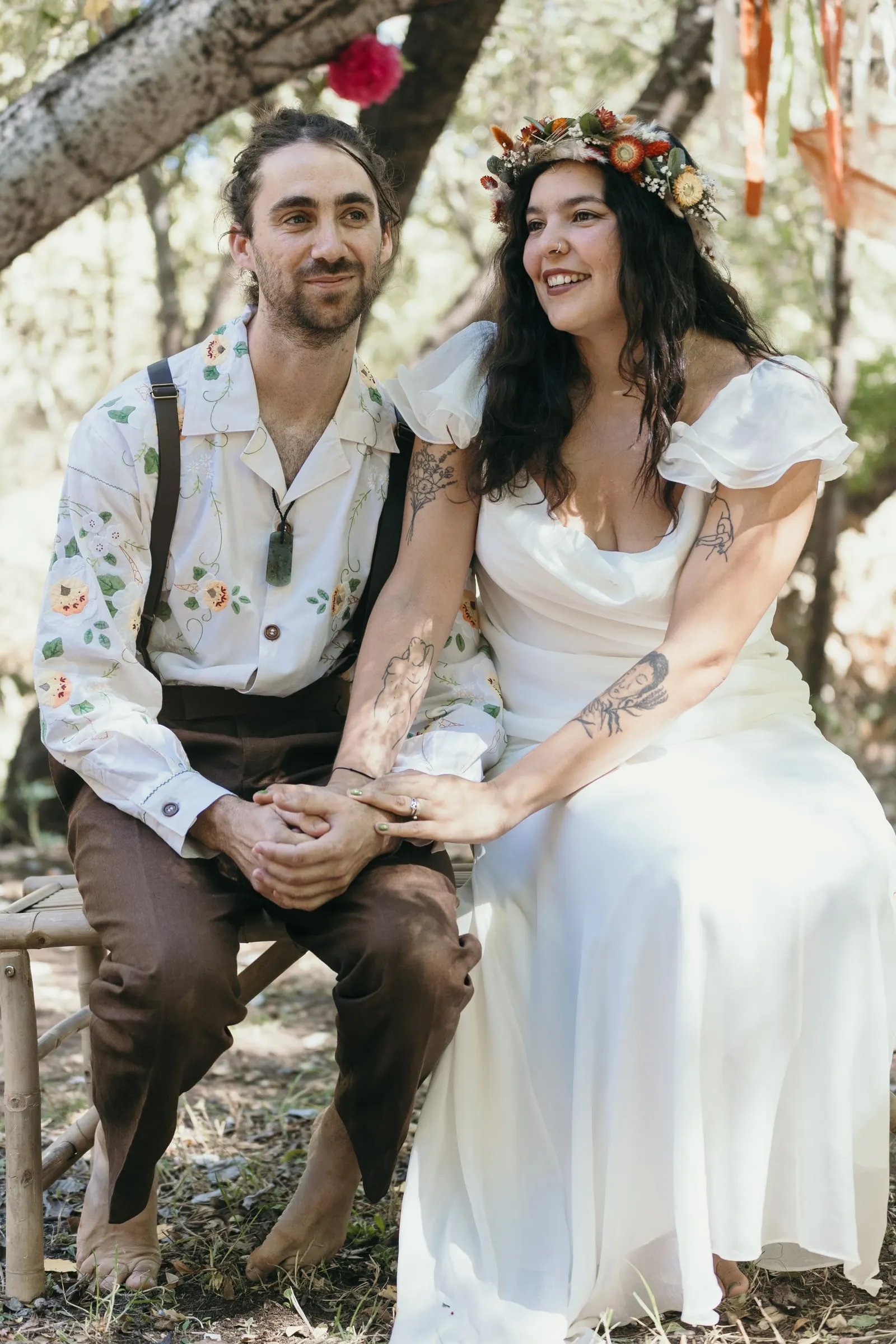 Couple holding hands on wooden stools at their woodland ceremony