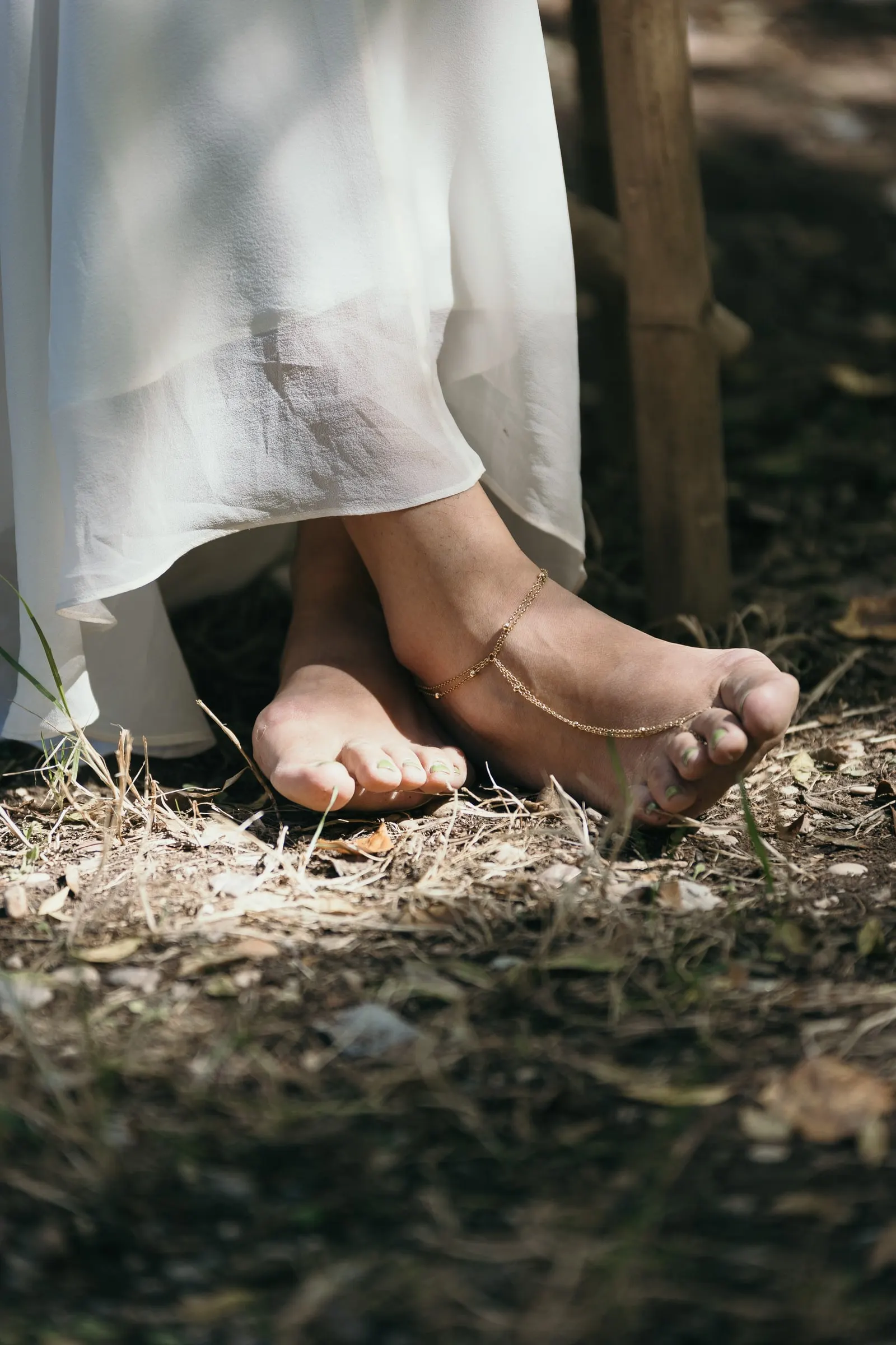 Bride's bare feet with an anklet on the dry grass