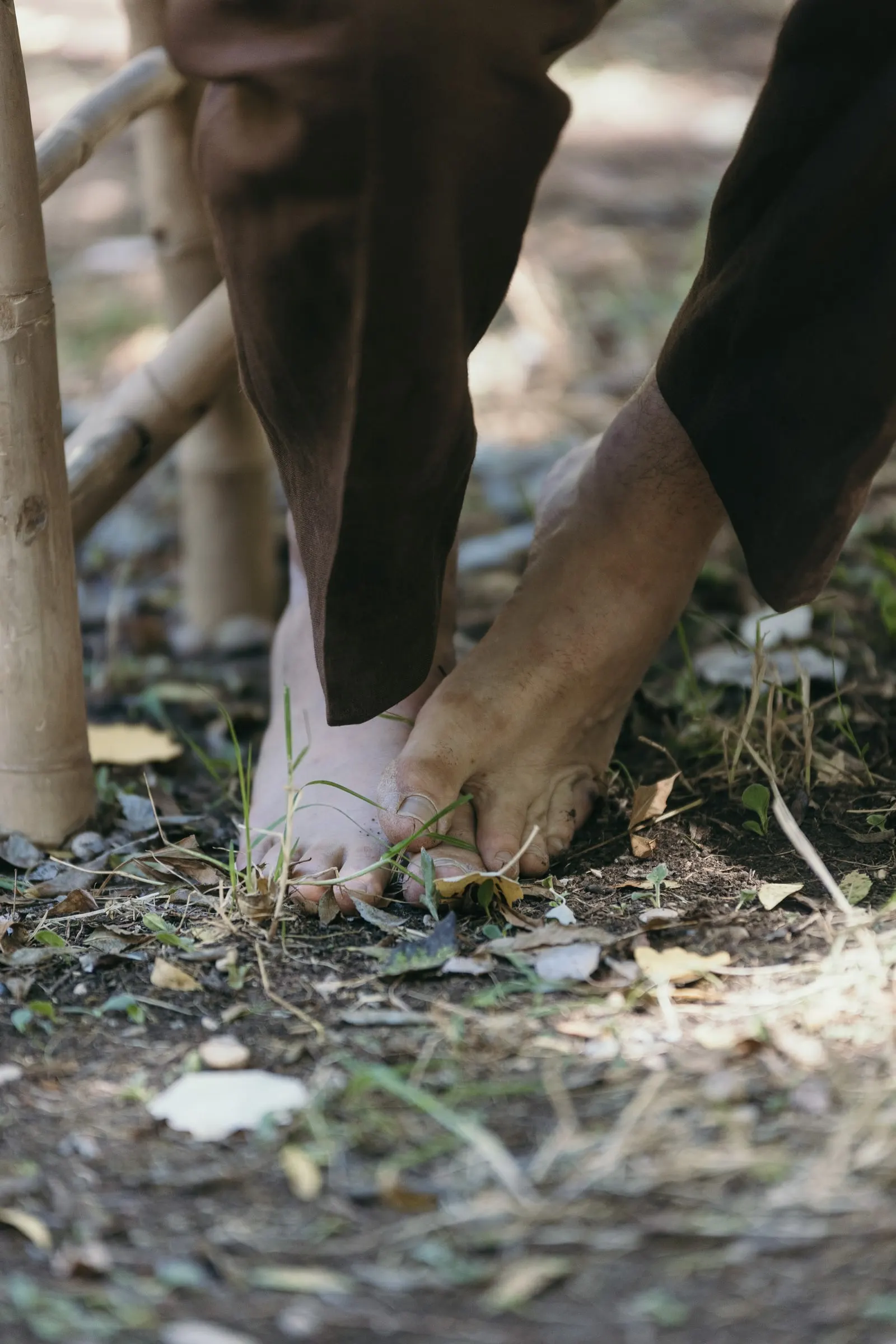 Groom's bare feet beside a bamboo bench at the ceremony