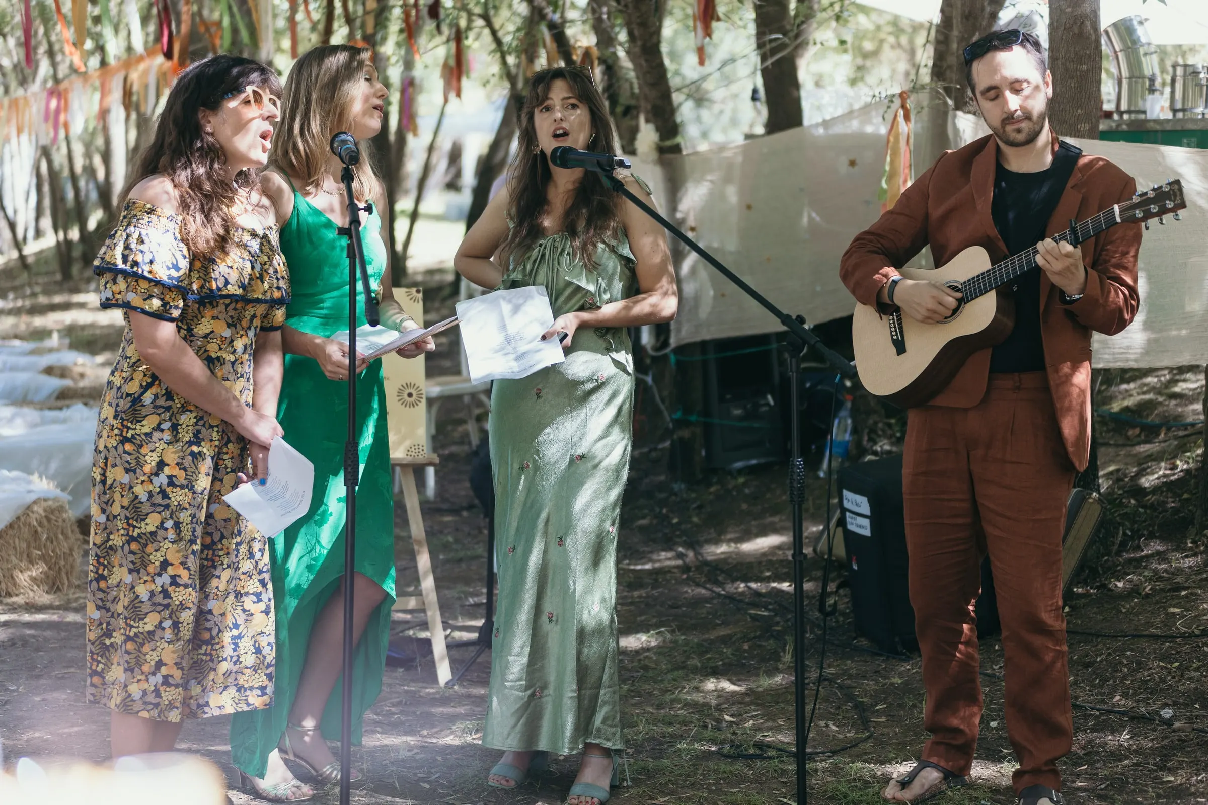 Friends singing to the couple at a microphone with a guitarist in a rust suit