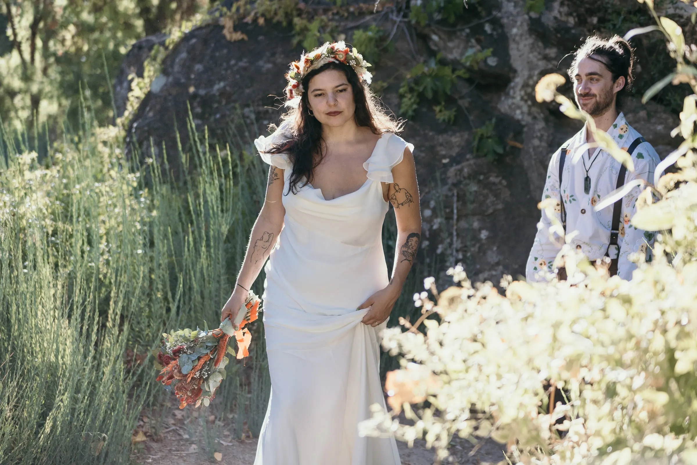 Bride walking through wild grasses by a boulder, the groom following