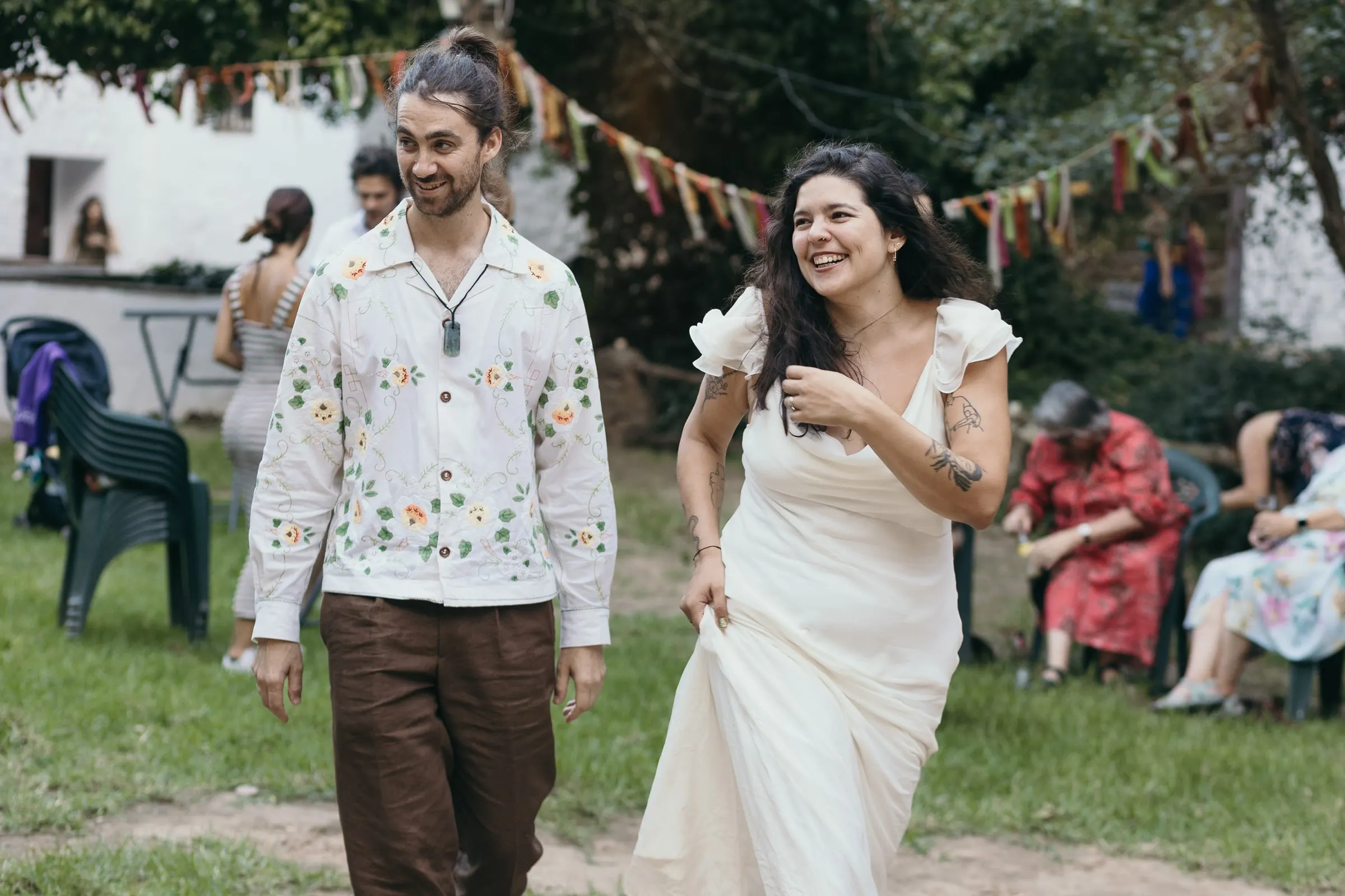 Couple crossing the lawn under bunting beside the whitewashed mill house
