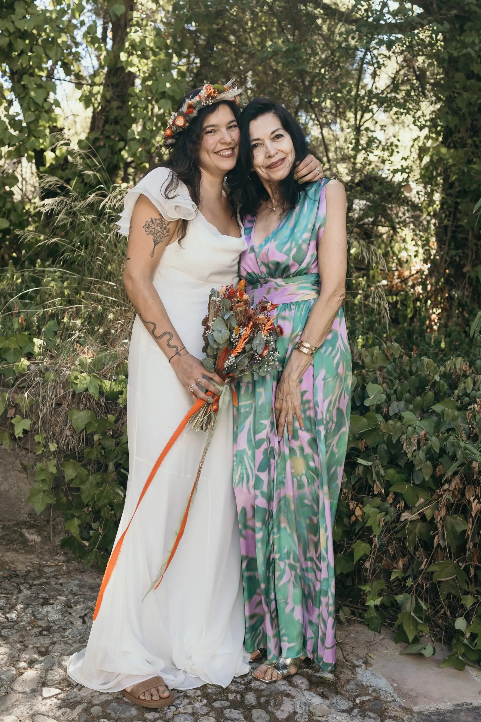 Bride and her friend in a floral jumpsuit leaning into each other among the trees of the Guadiaro valley