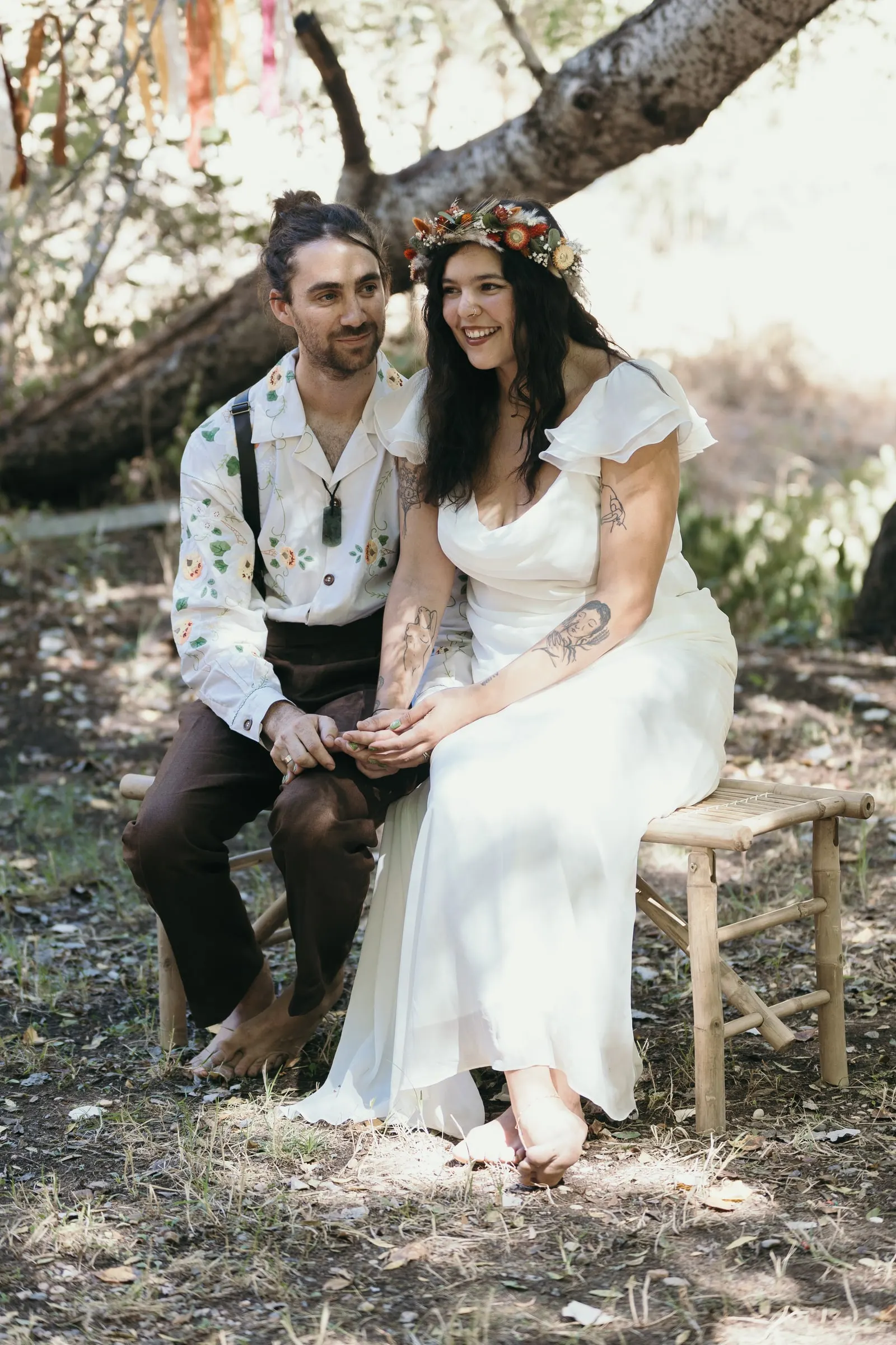 Bride and groom sitting side by side on a wooden bench, smiling during the woodland ceremony at Molino La Flor