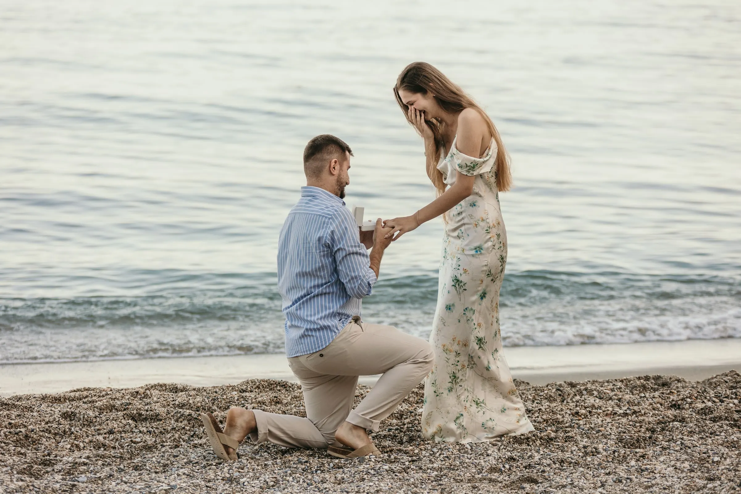 He kneels with the ring as she covers her face in surprise on the beach in Nerja