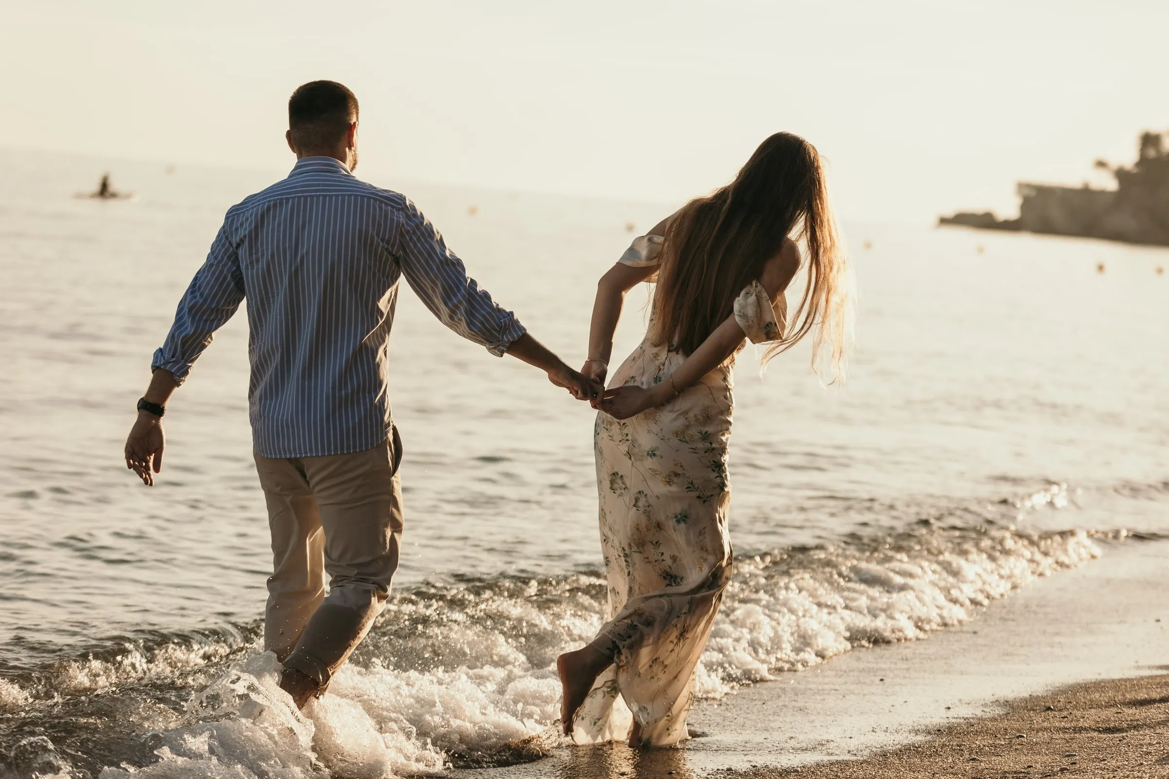 Couple running hand in hand into the waves, seen from behind, on the beach in Nerja