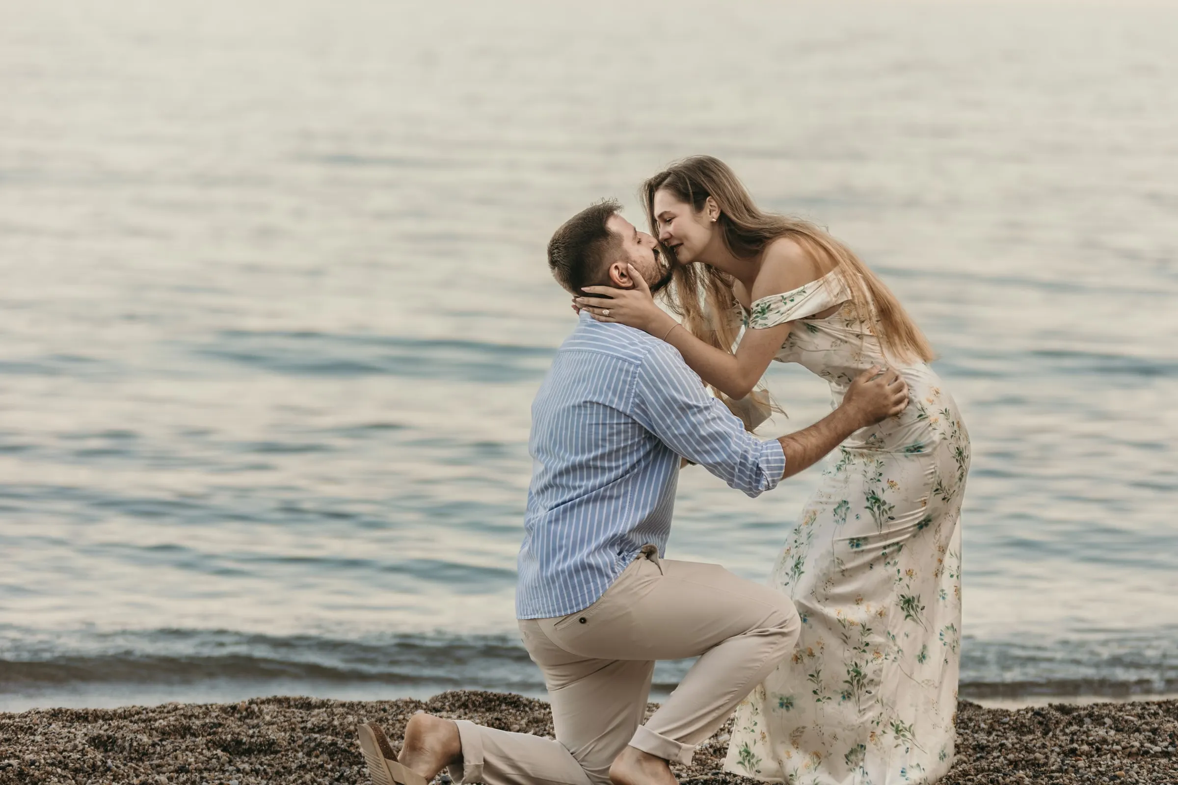 She leans down to kiss him while he is still on one knee, on the beach in Nerja